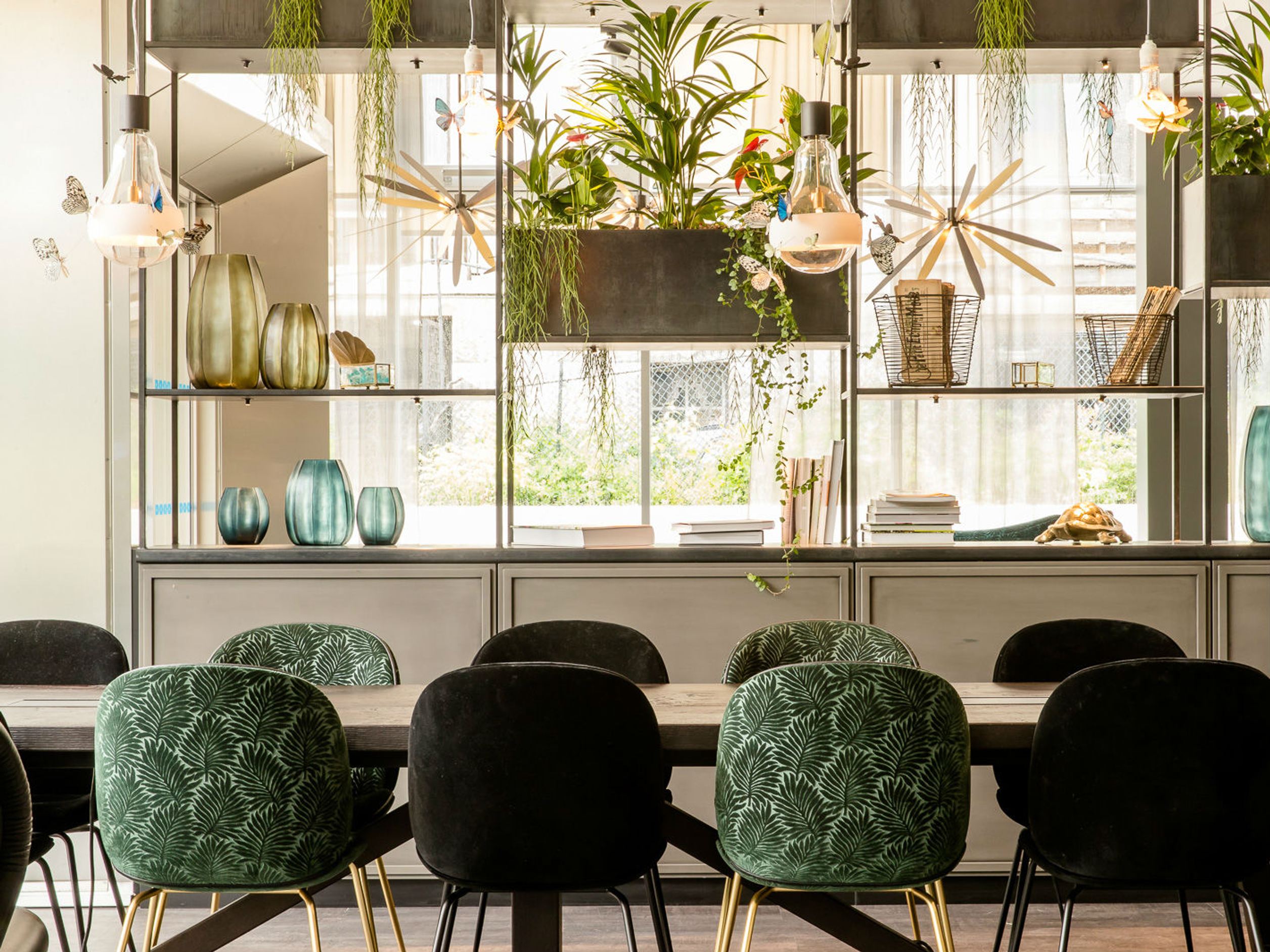 Motel One Essbereich mit stilvollen, gepolsterten Stühlen, viel natürlichem Licht und grünen Pflanzen