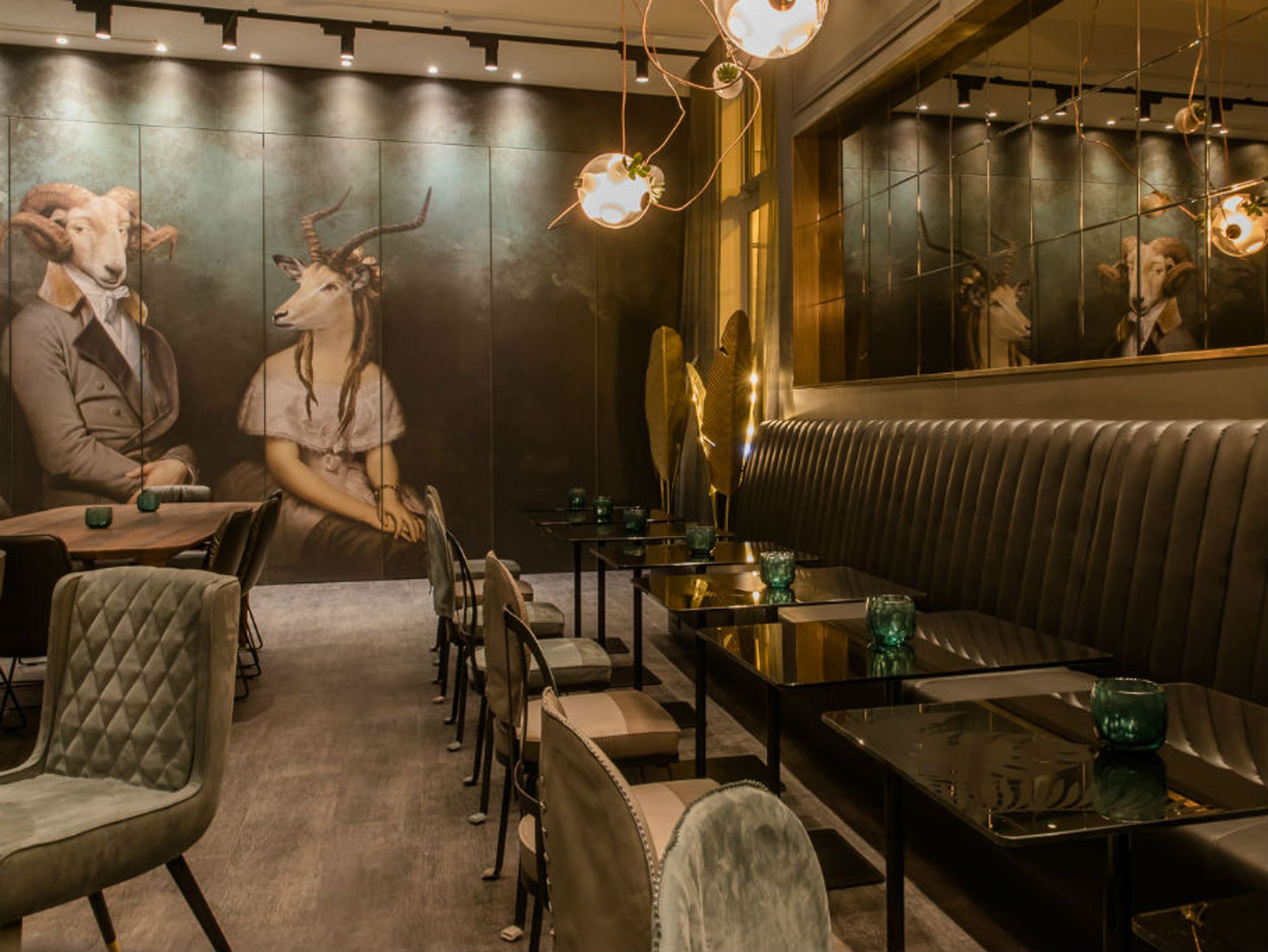 Motel One Restaurant mit gedämpfter Beleuchtung, stilvollen Sitzmöbeln und ungewöhnlicher Wandkunst: Porträts von Menschen mit Tierköpfen.
