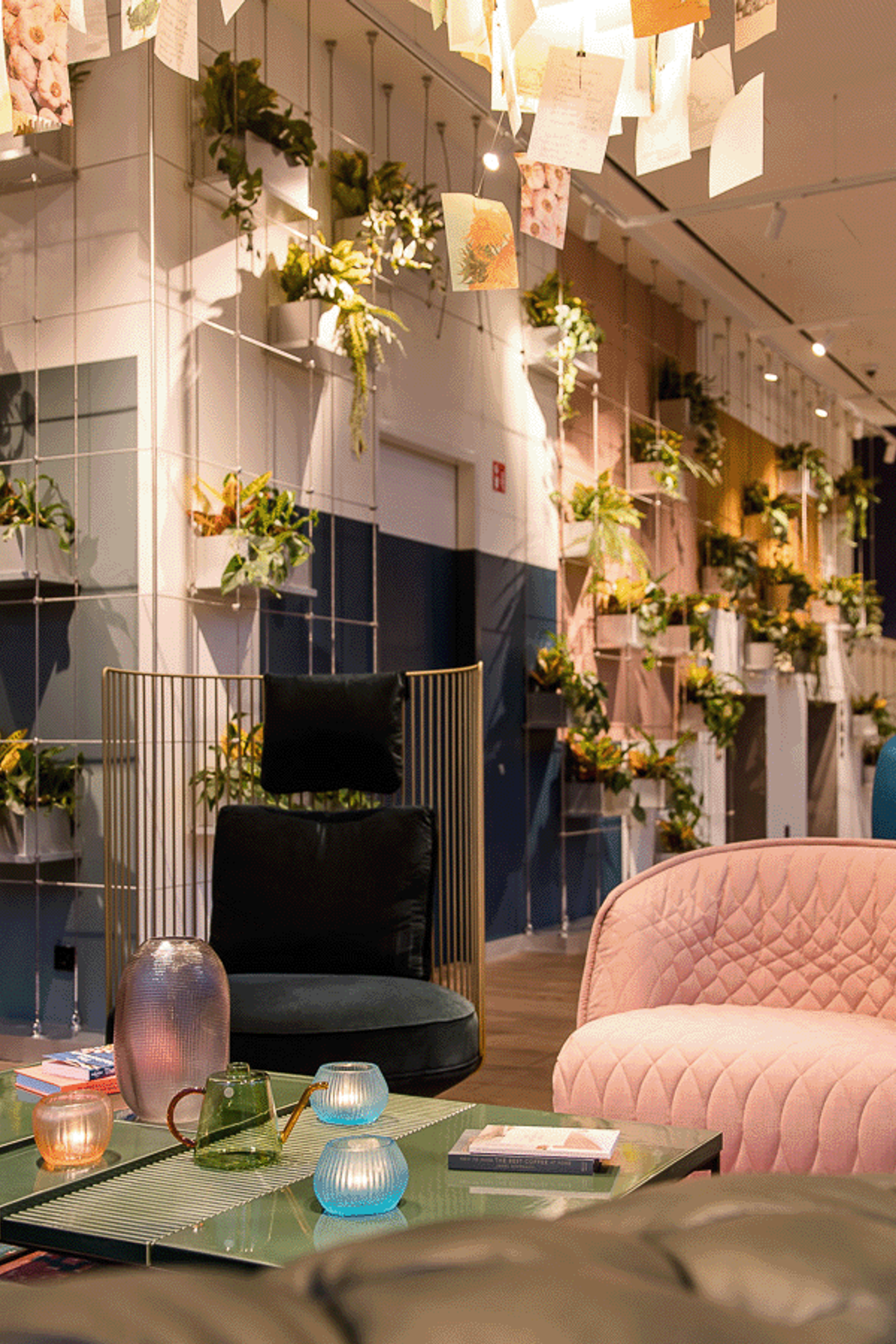 Motel One Hotel-Loungebereich mit modernen, farbenfrohen Sesseln, grünen Pflanzen an der Wand und einem dekorativen Kamin, der Wärme und Entspannung ausstrahlt.