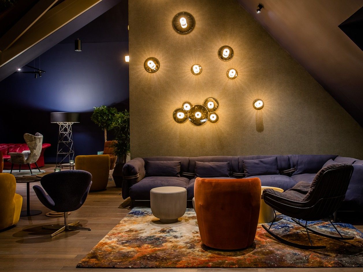 Gemütlicher Lounge-Bereich mit stilvollen Sesseln, Sofas und warmem Licht an einer schrägen Wand.