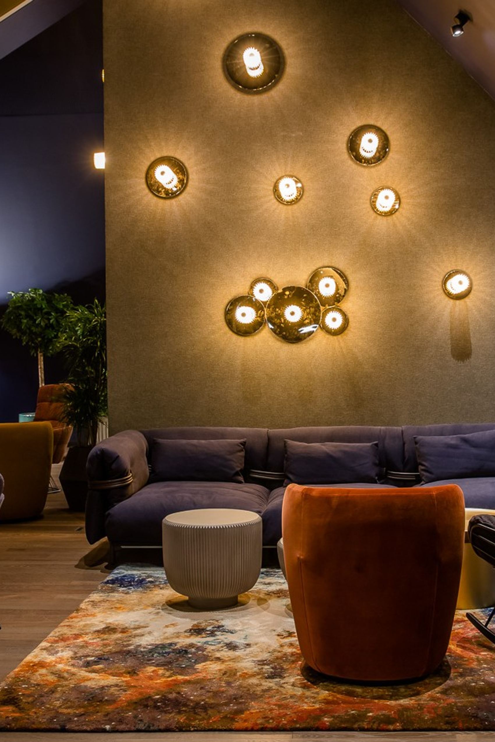 Gemütlicher Lounge-Bereich mit stilvollen Sesseln, Sofas und warmem Licht an einer schrägen Wand.