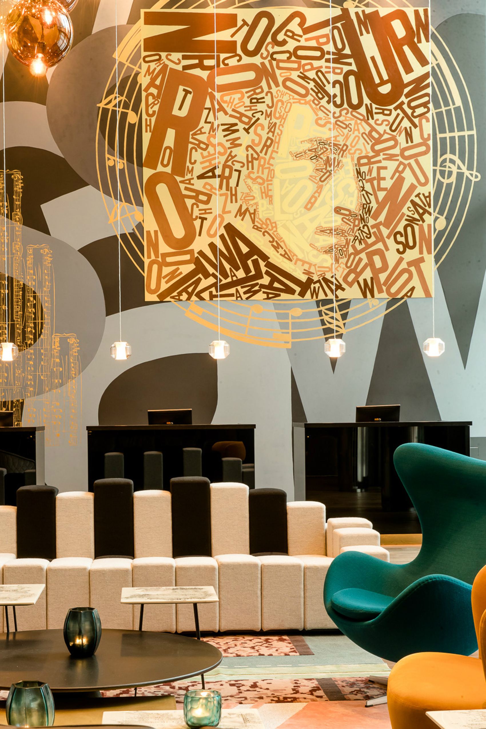 Motel One Hotel-Lobbybereich mit stilvollen Sitzmöbeln in Schwarz, Weiß und Grün, einer großen dekorativen Wandkunst aus Buchstaben.