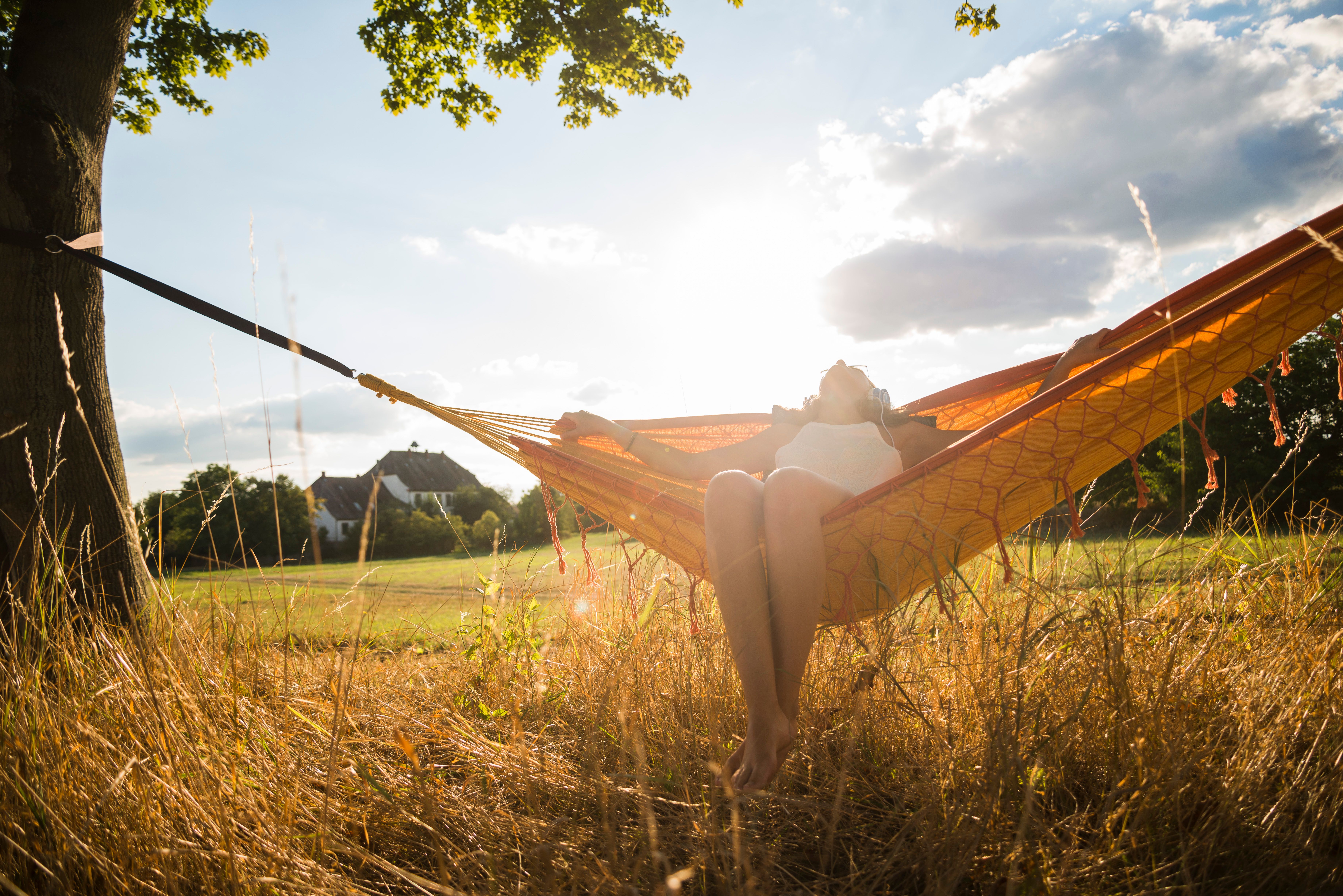 Hotel Motel One Blaue Pause Person entspannt in Hängematte unter Baum, umgeben von sonniger, offener Natur mit Wiesen und blauem Himmel.