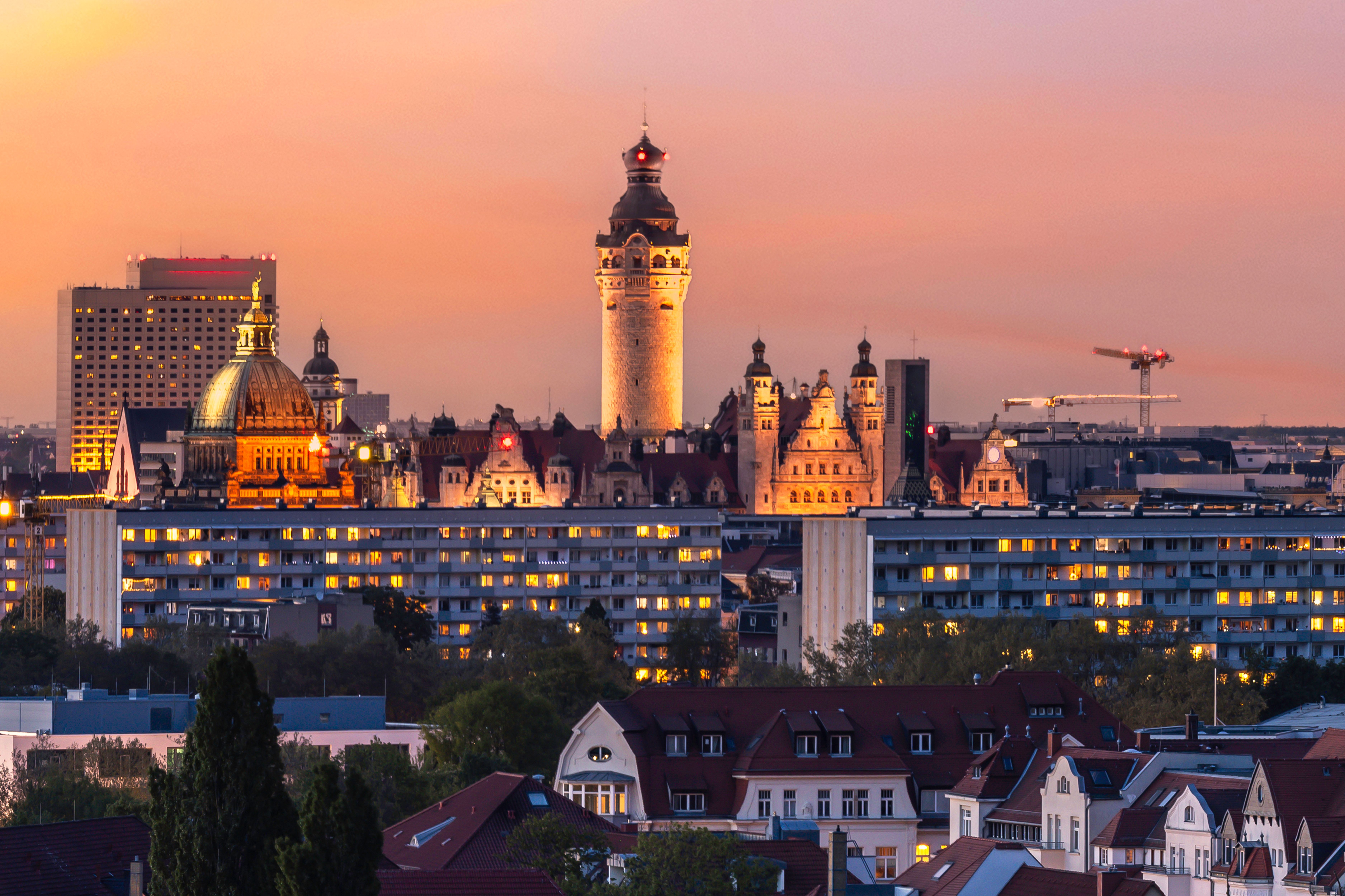 Abendliche Stadtansicht mit historischen Türmen und beleuchteten Gebäuden, die eine harmonische Verbindung von Alt und Neu im urbanen Panorama zeigen.