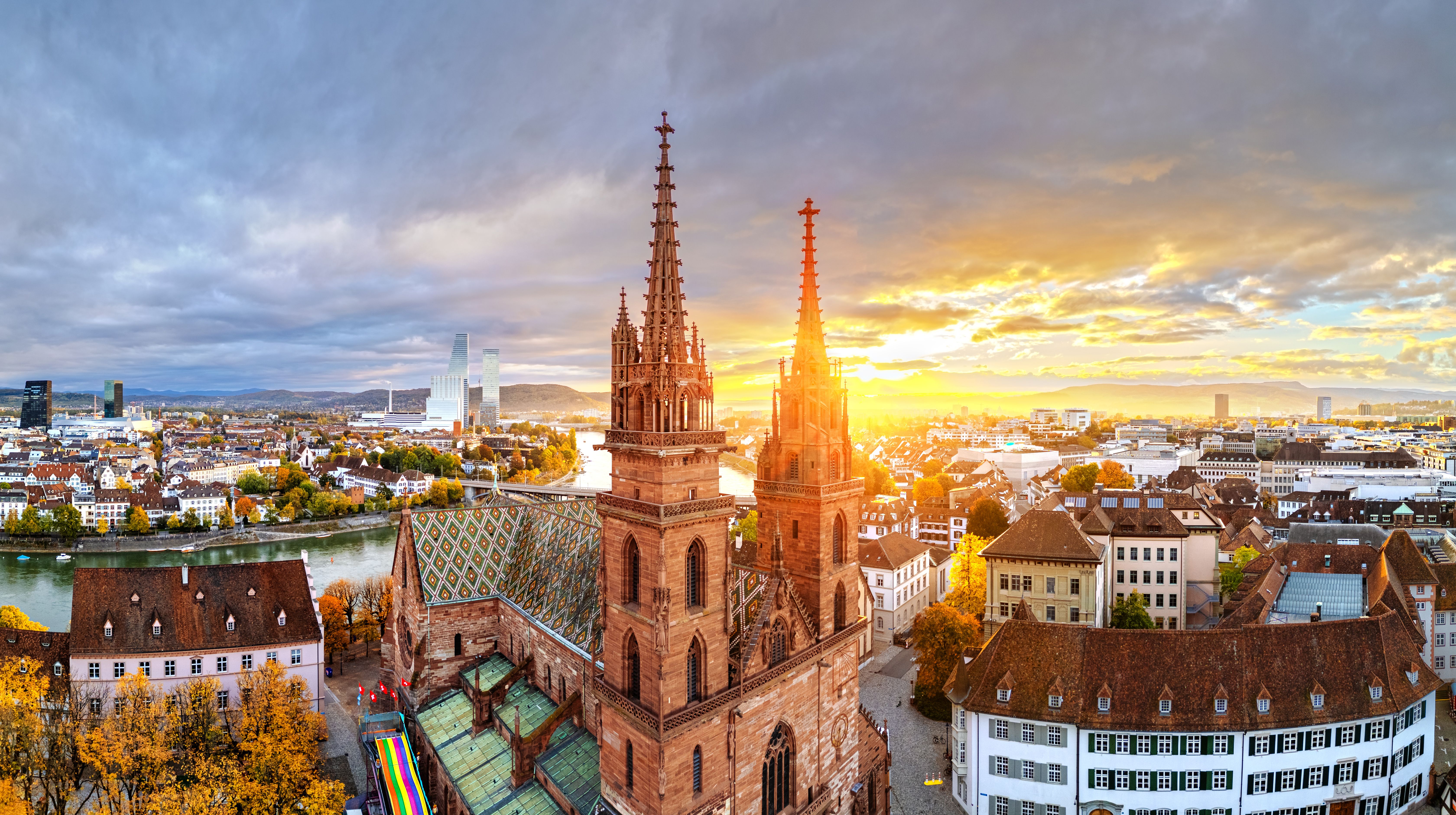 Sonnenuntergang über der historischen Altstadt mit markanter gotischer Kirche und bunten Herbstbäumen, die eine warme und einladende Atmosphäre schaffen.