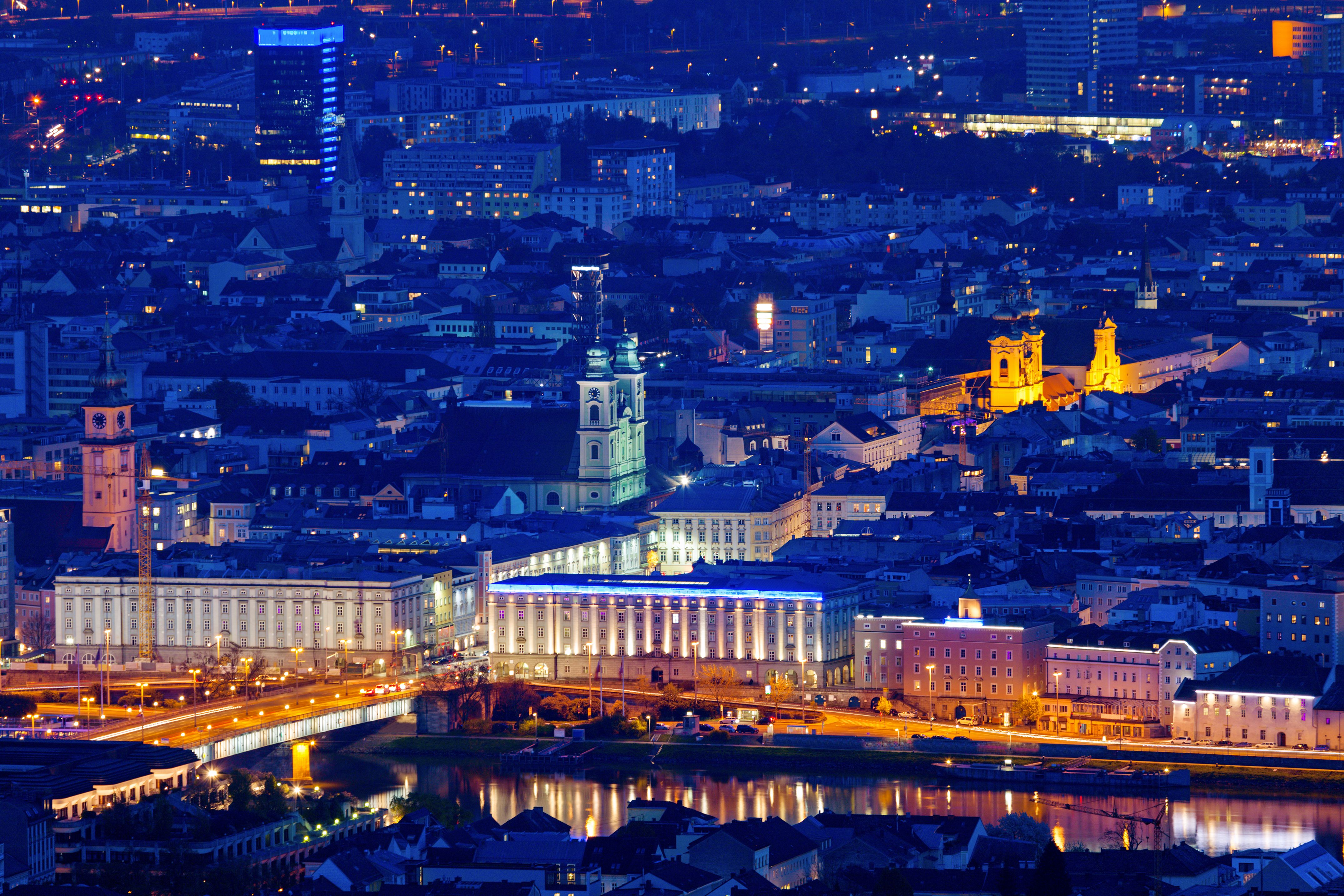 Nachtblick auf eine lebendige Stadt mit beleuchteten historischen Gebäuden, Brücken und Fluss, die eine harmonische Verbindung von Tradition und Moderne zeigen.
