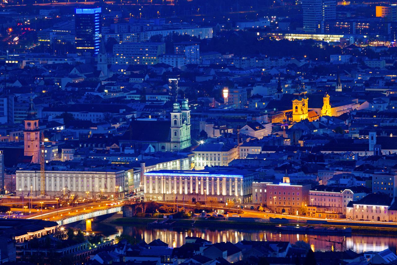 Nachtblick auf eine lebendige Stadt mit beleuchteten historischen Gebäuden, Brücken und Fluss, die eine harmonische Verbindung von Tradition und Moderne zeigen.