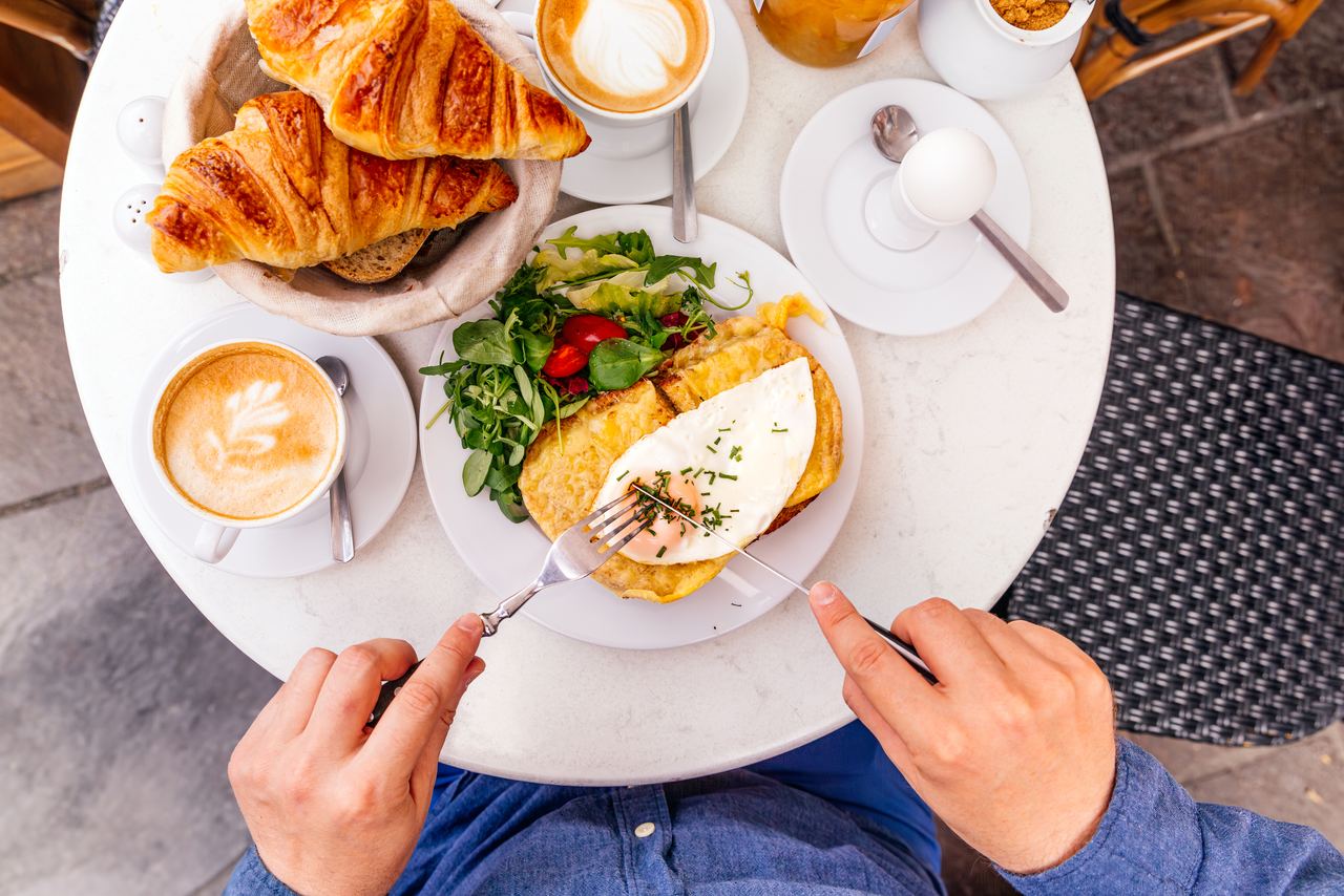 Frühstückstisch mit frischen Croissants, Cappuccino, Omelett mit Spiegelei und Salat, gekochtem Ei, serviert in heller, einladender Atmosphäre.