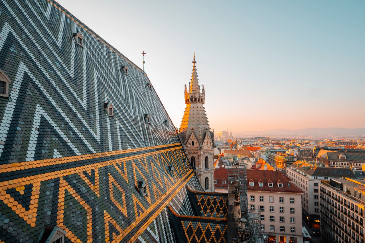 Dach des Stephansdoms in Wien mit bunten Ziegelmustern und Turm im Abendlicht, Blick über die Stadt mit historischen Gebäuden und sanftem Himmel. Dach des Stephansdoms in Wien mit bunten Ziegelmustern und Turm im Abendlicht, Blick über die Stadt mit historischen Gebäuden und sanftem Himmel.