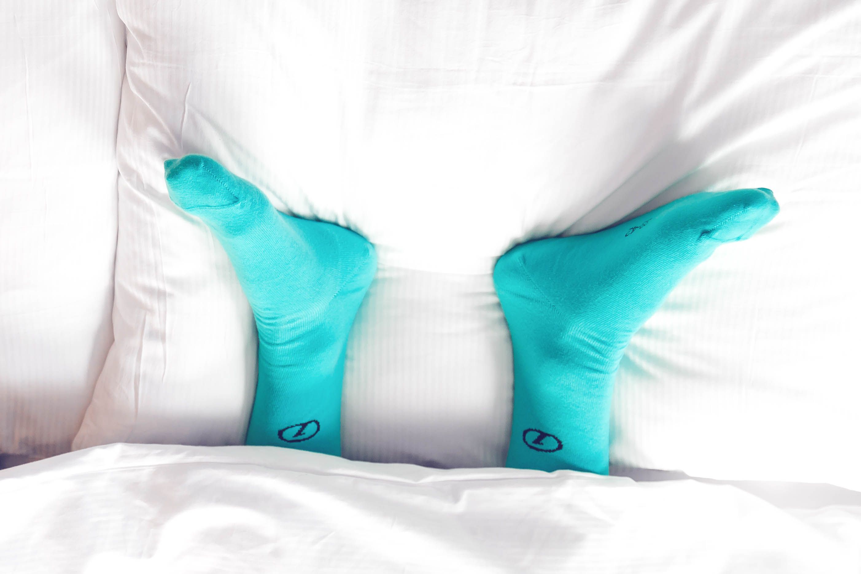 Zwei Füße mit türkisen Socken schauen unter einer Bettdecke hervor Motel One Hotels