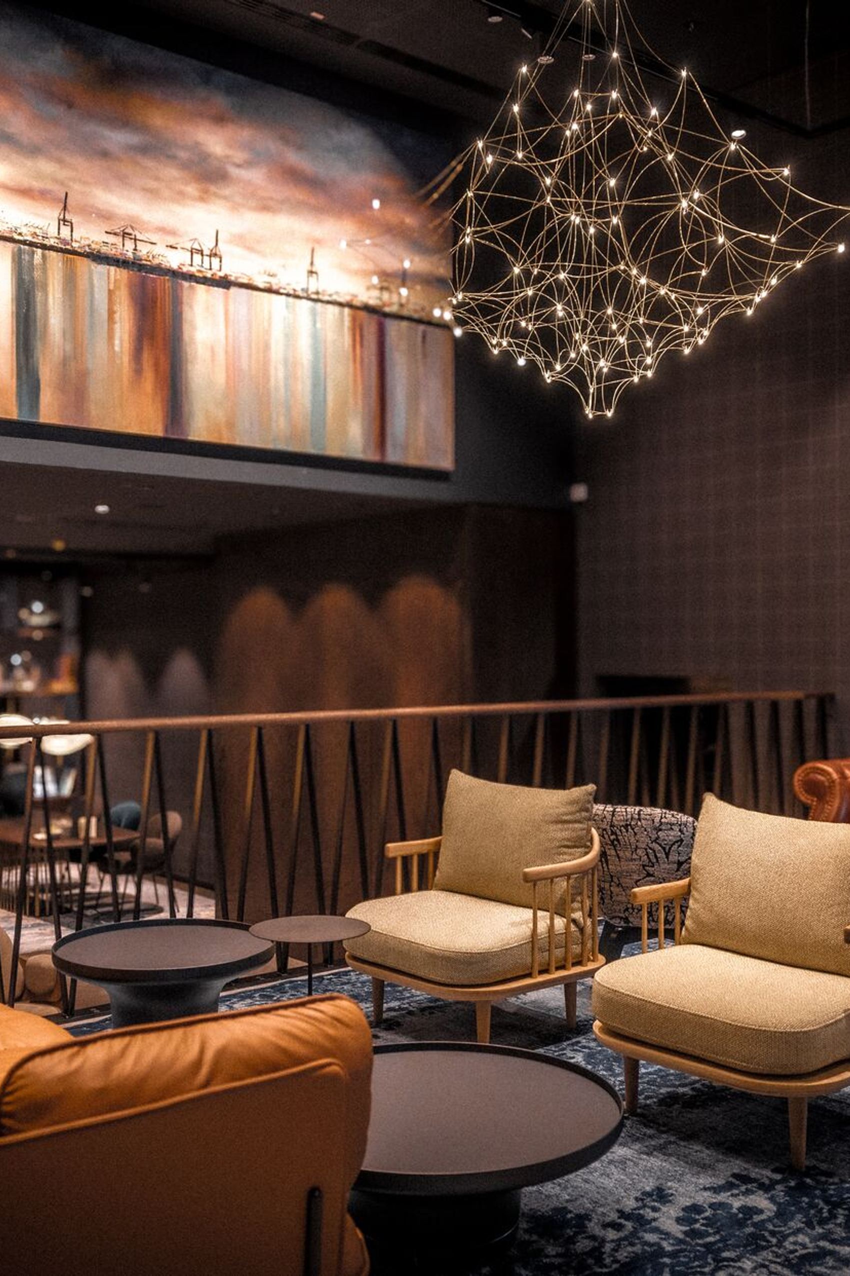 Motel One Lounge-Bereich mit modernen Sesseln, braunem Ledersofa und filigraner Hängeleuchte, warm beleuchtet