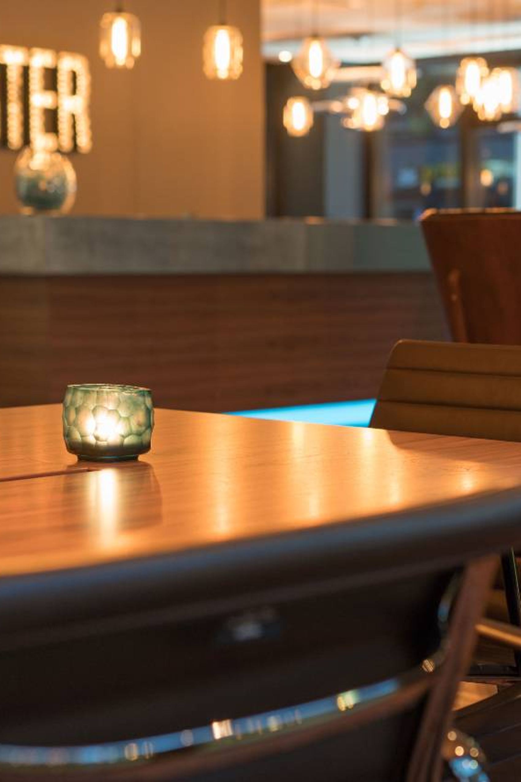 Motel One Aufenthaltsbereich mit stilvollen Ledersesseln und warmem Kerzenlicht auf dem Holztisch, gemütliche Atmosphäre in entspannter Lounge mit gedämpfter Beleuchtung und Dekoration.