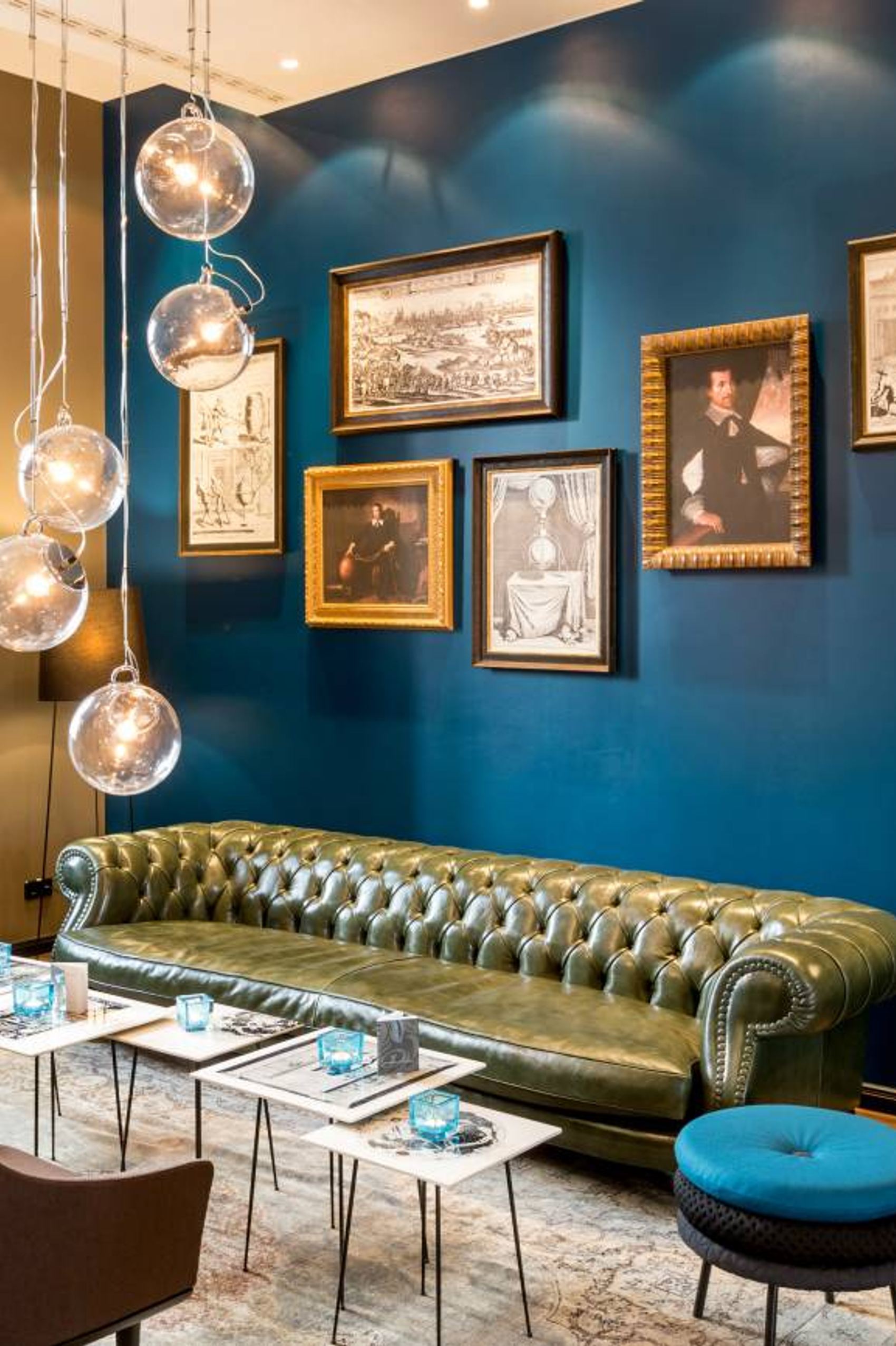 Gemütliche Lounge mit grünem Chesterfield-Sofa, stilvoller Beleuchtung und historischen Bildern an dunkelblauer Wand