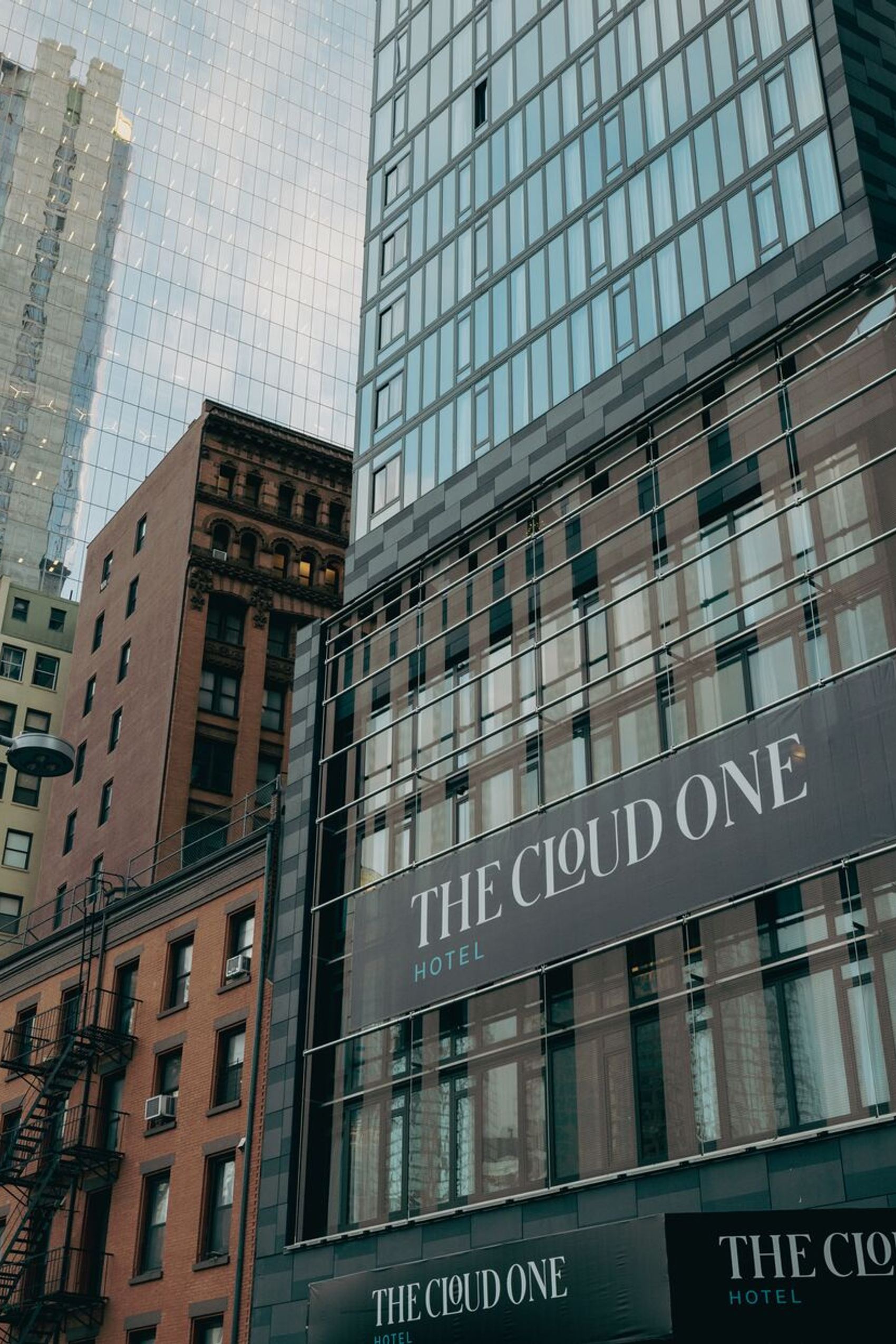 Hochhausfassade eines modernen Hotels mit dem Schriftzug „THE CLOUD ONE“, umgeben von verschiedenen Gebäuden in der Stadt.