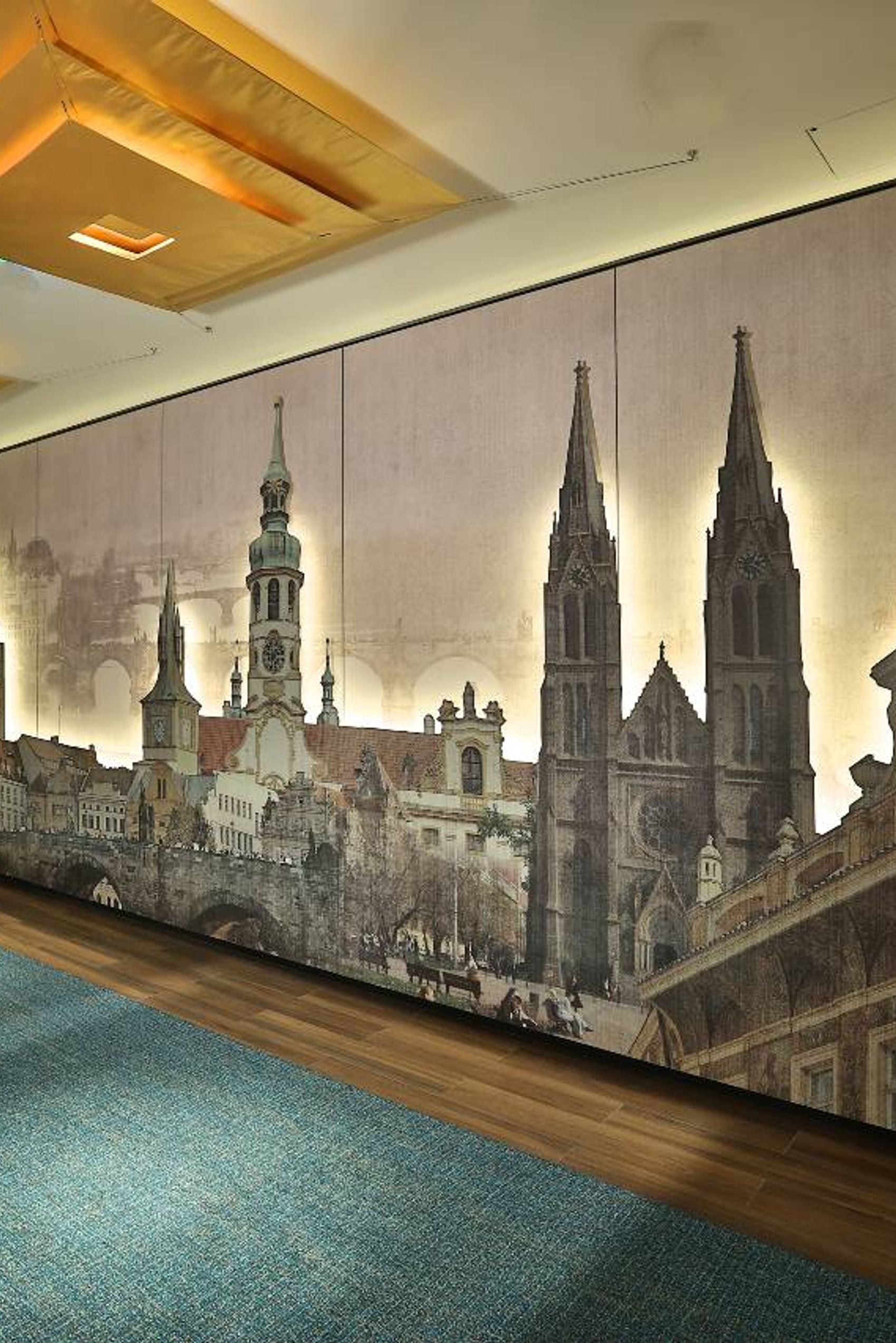 Wandbild eines historischen Stadtpanoramas mit markanten Kirchtürmen und alten Gebäuden, stimmungsvoll beleuchtet in einem Flur mit Holzfußboden und blauen Teppichläufern.