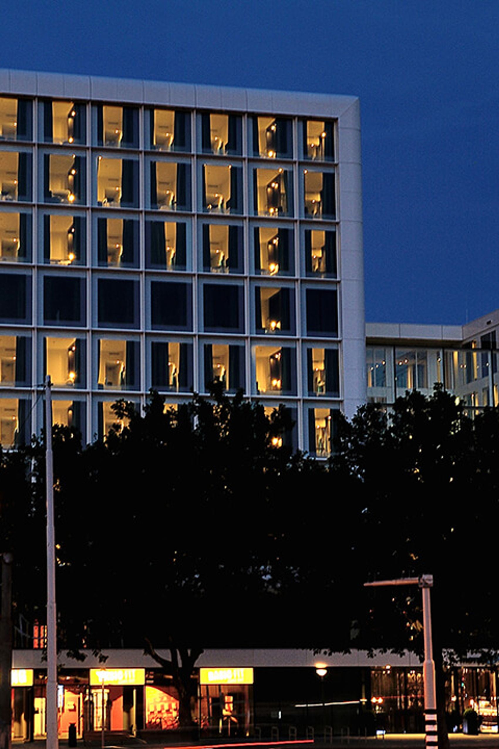 Motel One Hotel bei Abenddämmerung, beleuchtete Fenster, klare Architektur.