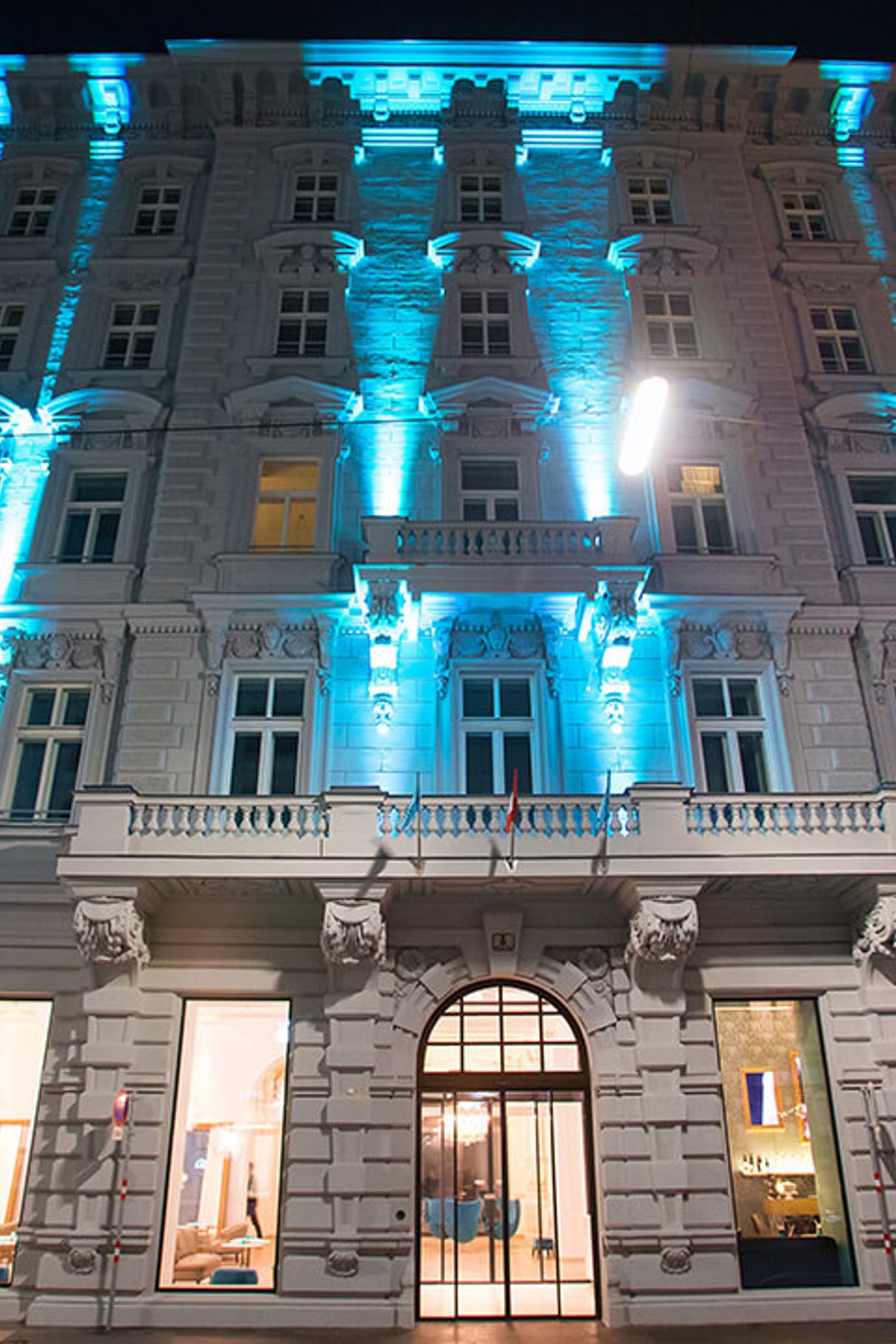 Fassade eines Hotels mit historischer Architektur, beleuchtet mit sanftem blauem Licht. Eingangsbereich mit großen Fenstern und sichtbarem Empfangsbereich.