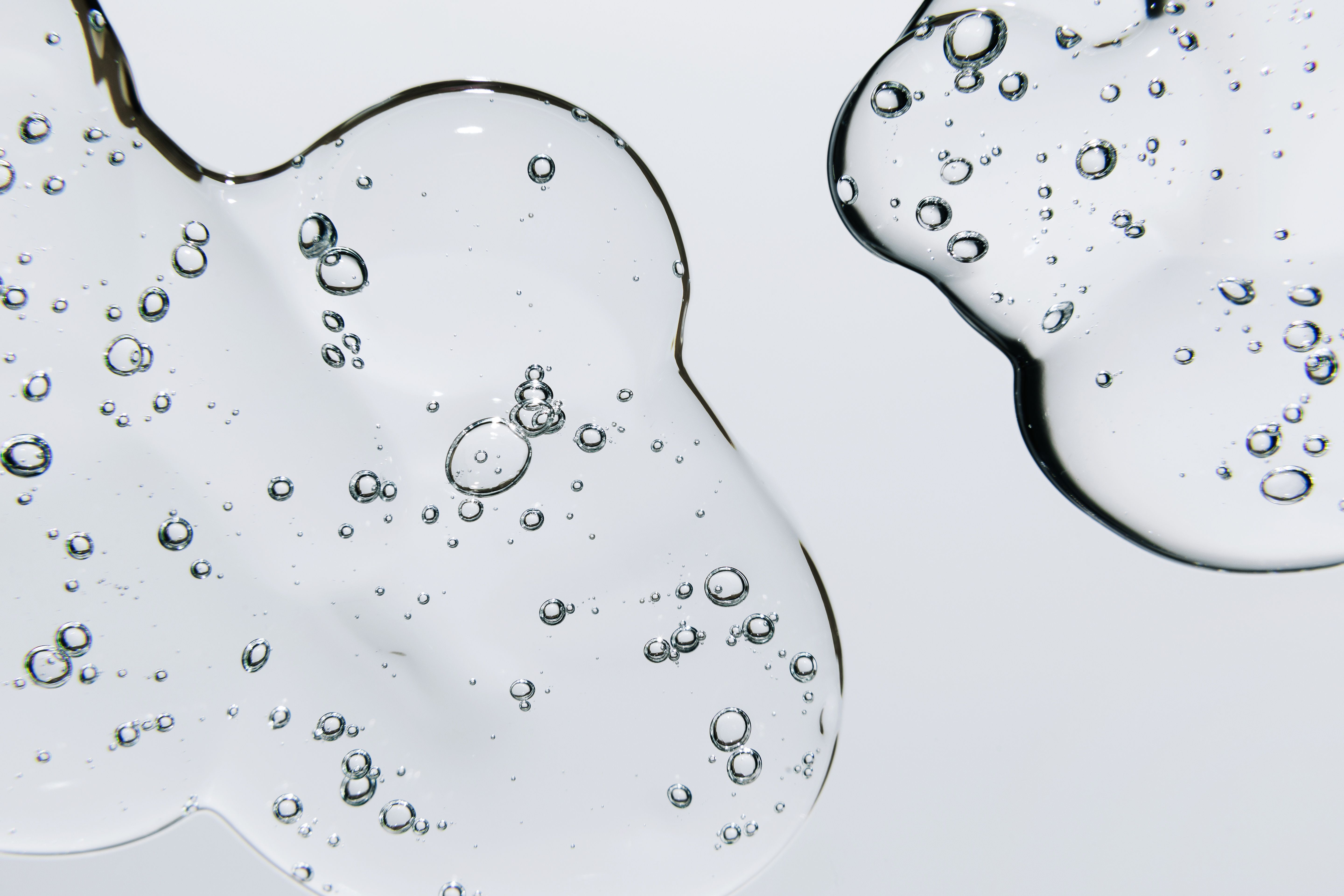 Nahaufnahme von klaren, transparenten Gel-Tropfen mit eingeschlossenen Luftblasen auf hellem Hintergrund, die Frische und Reinheit symbolisieren.