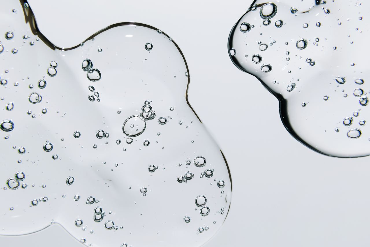Nahaufnahme von klaren, transparenten Gel-Tropfen mit eingeschlossenen Luftblasen auf hellem Hintergrund, die Frische und Reinheit symbolisieren.
