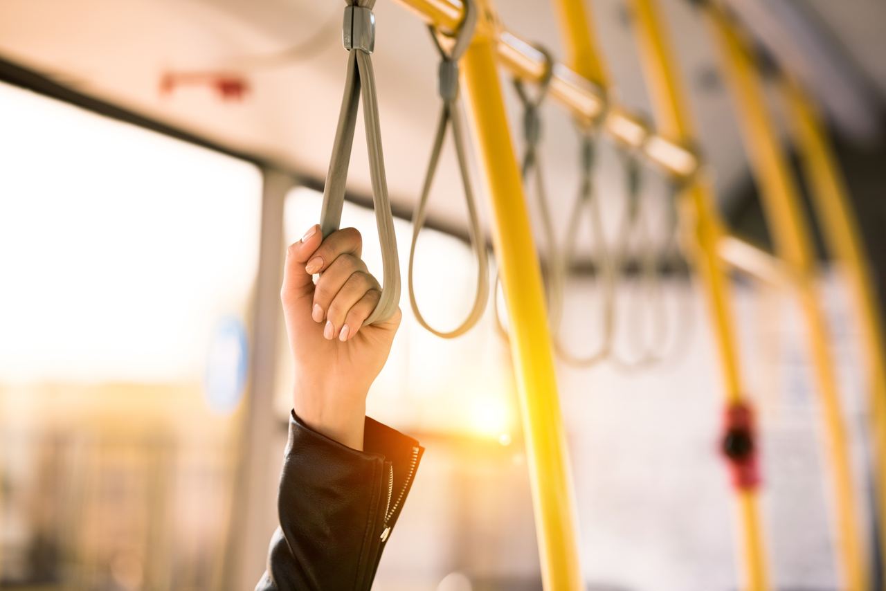 Hand hält sich an einer Halteschlaufe in einem öffentlichen Verkehrsmittel, warmes Licht beleuchtet den Hintergrund, symbolisiert Mobilität und Komfort während der Reise.