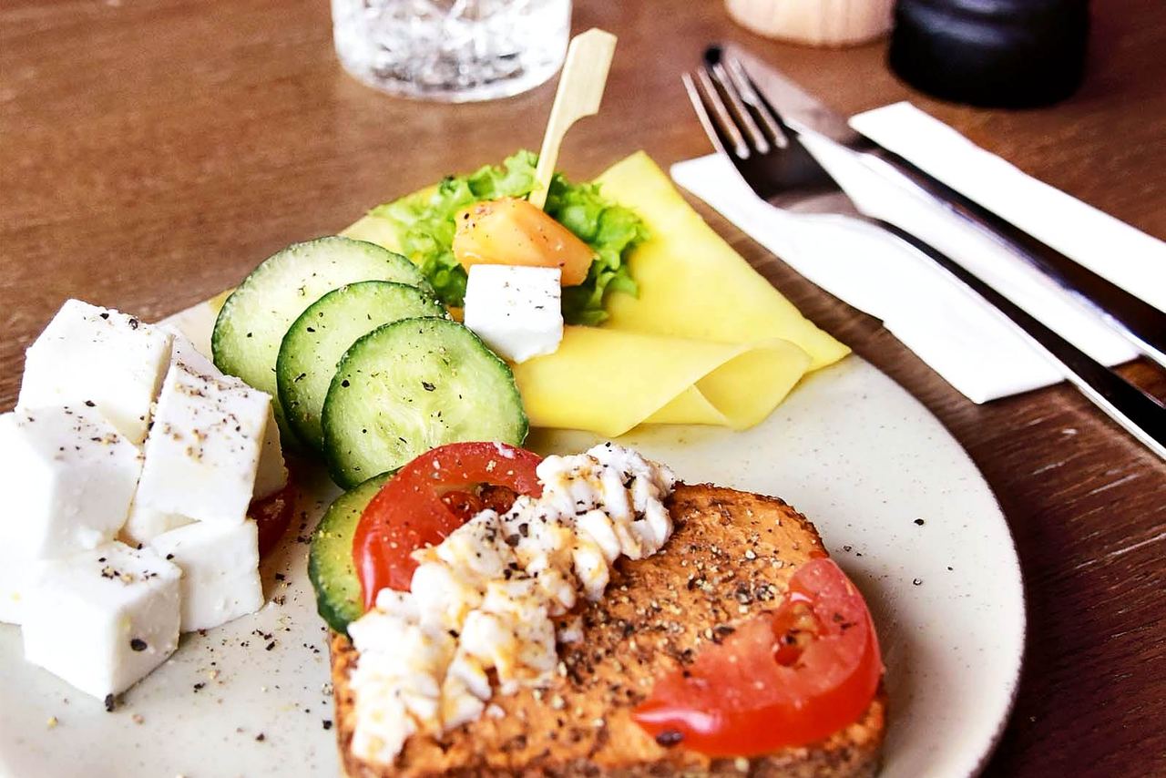 Frischer Frühstücksteller mit Feta, Gurkenscheiben, Tomaten, Salat, Käse und Vollkornbrot, appetitlich angerichtet, ideal für einen gesunden Start in den Tag.