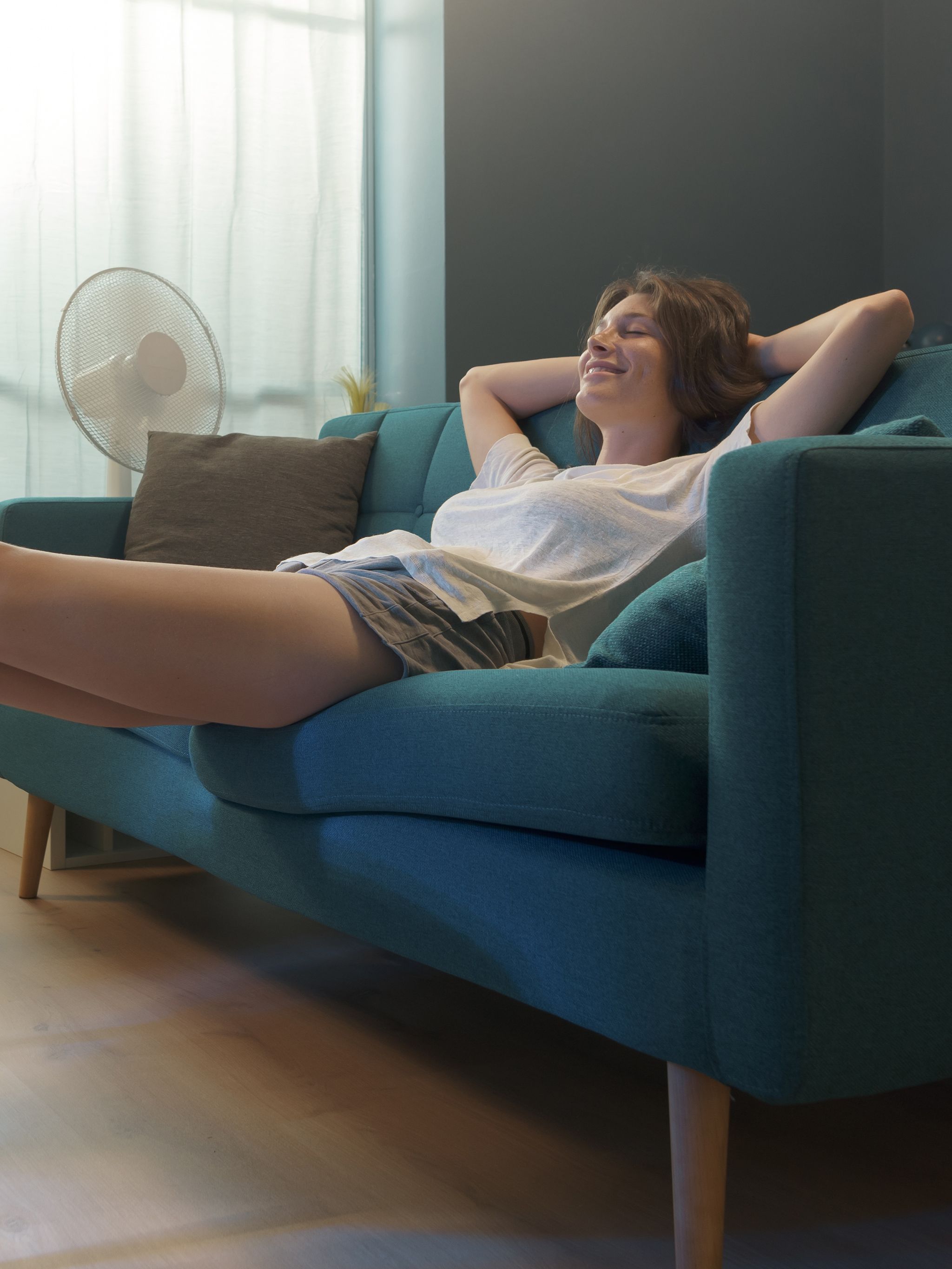 Frau entspannt sich auf einem Sofa, legt ihre Füße auf einen Tisch vor einem offenen Kühlschrank und genießt eine ruhige, gemütliche Atmosphäre im Wohnzimmer.