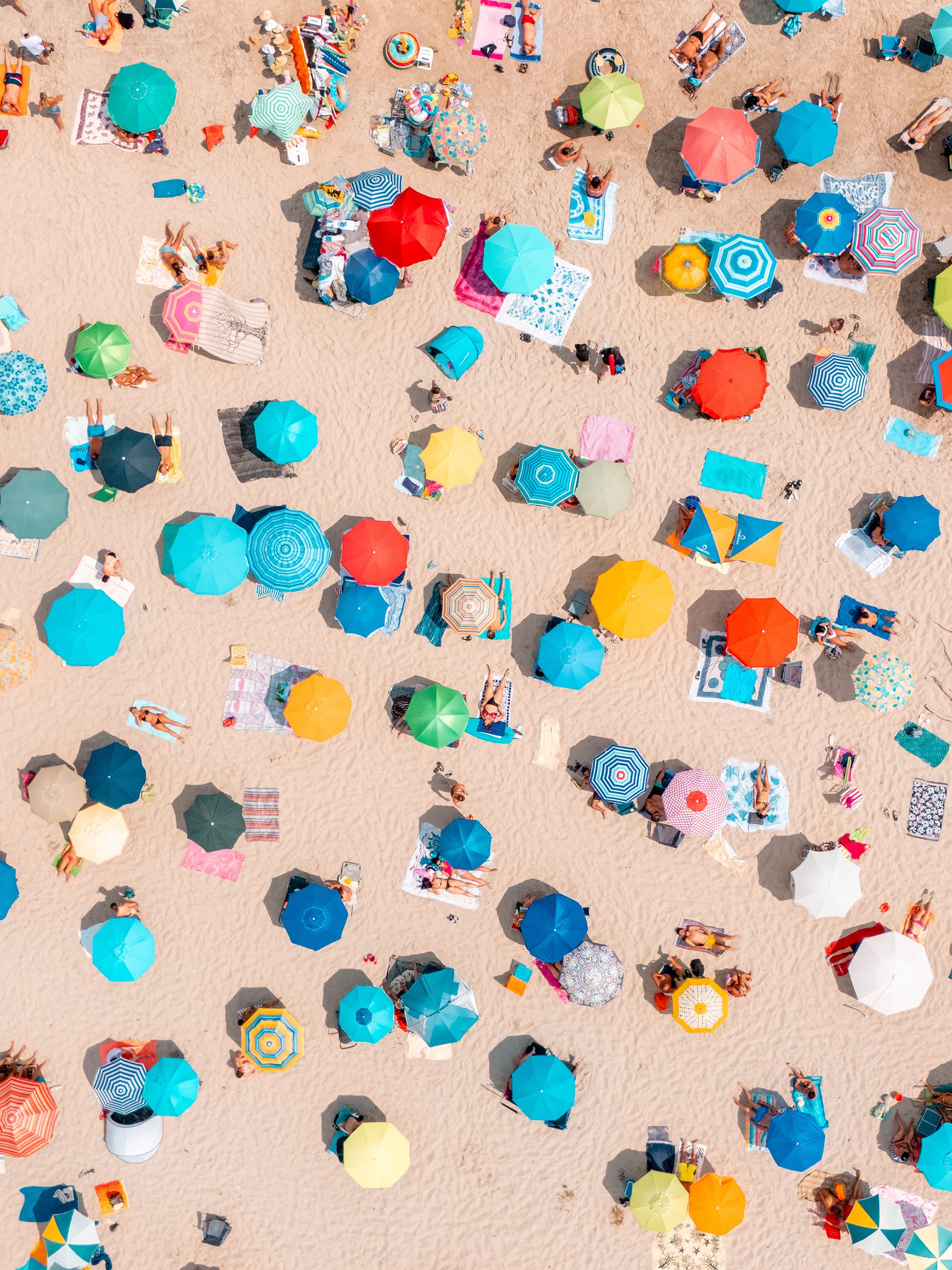 Luftaufnahme eines belebten Sandstrandes mit bunten Sonnenschirmen und Menschen, die Sonne und Meer genießen.