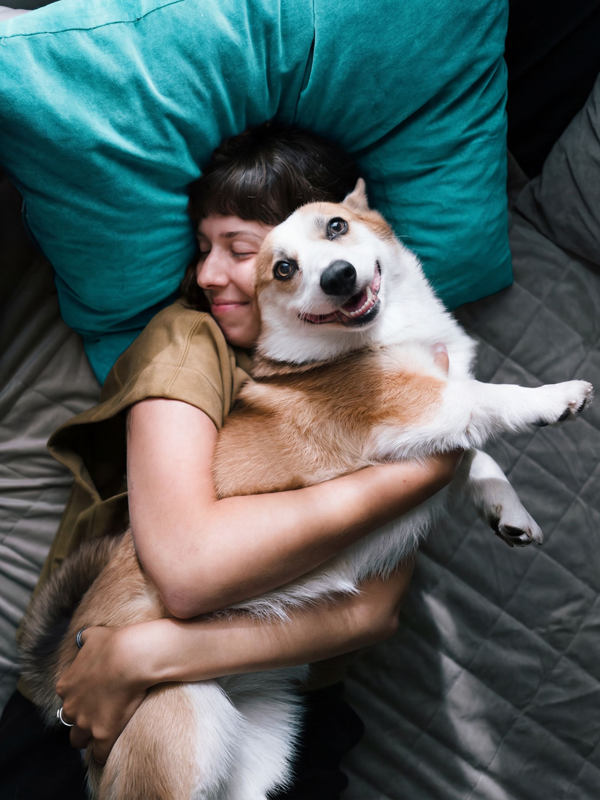 Frau liegt entspannt auf einem Sofa und umarmt liebevoll einen zufriedenen Hund, vermittelt Geborgenheit und Wärme.