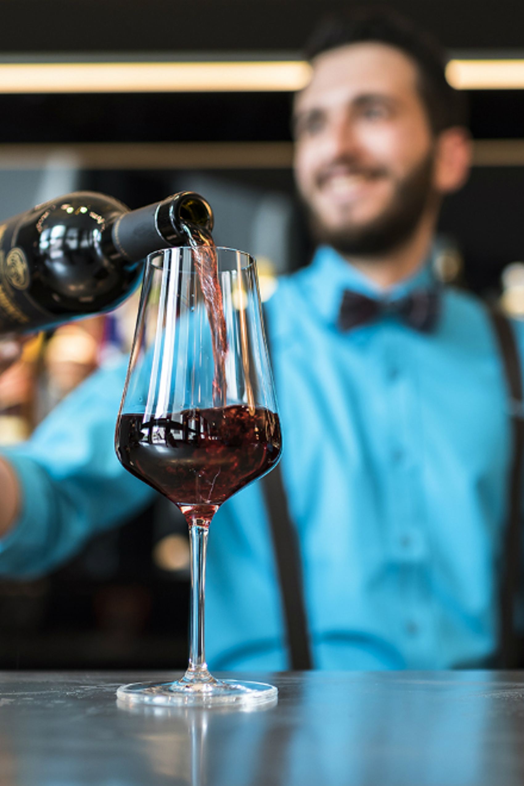 Ein Barkeeper in blauem Hemd füllt ein Glas mit rotem Wein, der Fokus liegt auf dem Glas, das stilvoll eingeschenkt wird.