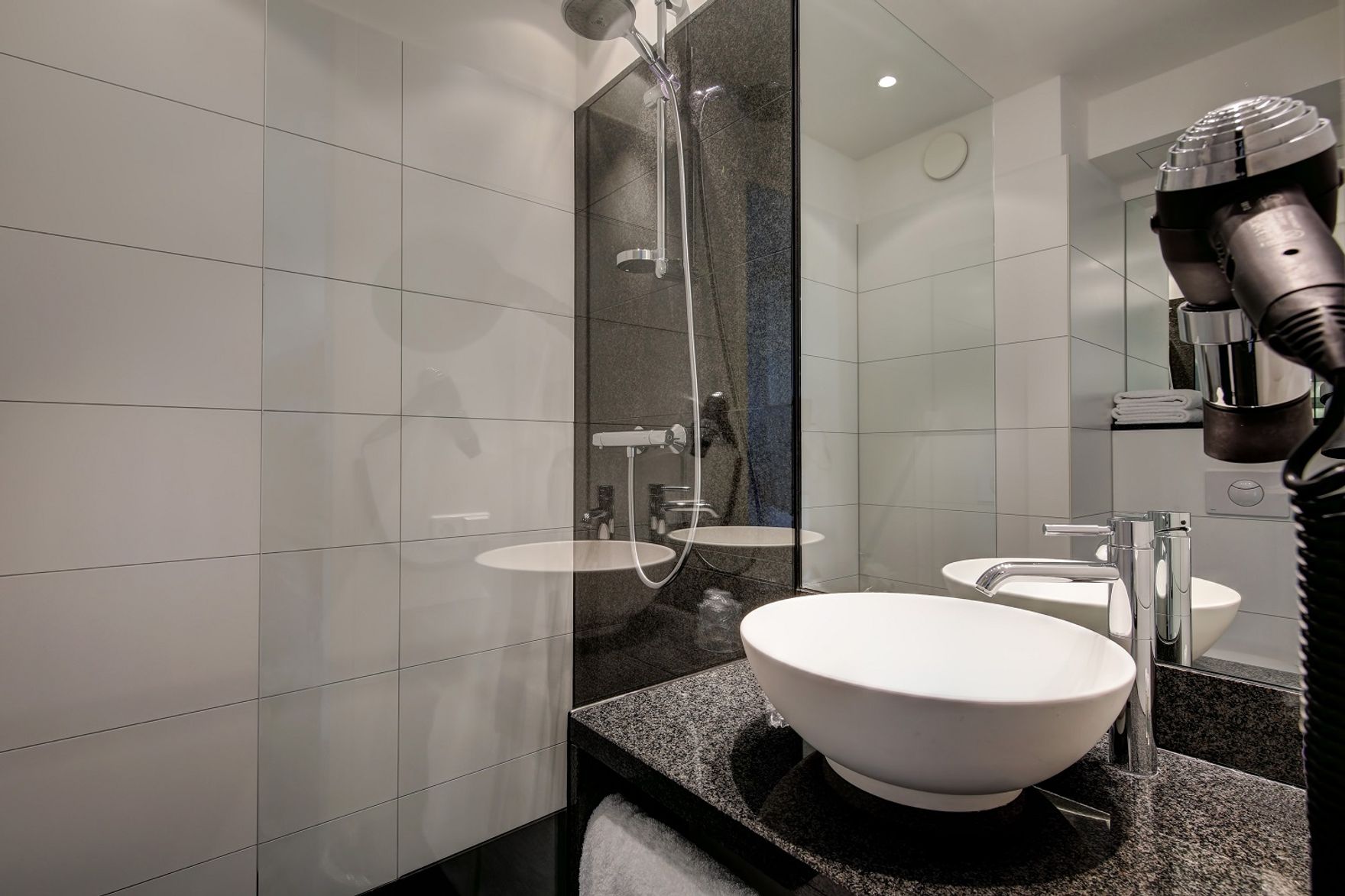 Hotelbadezimmer mit großzügiger Dusche, rundem Waschbecken auf Granitplatte und Haartrockner an der Wand, ideal für komfortable Erfrischung und Pflege während des Aufenthalts.