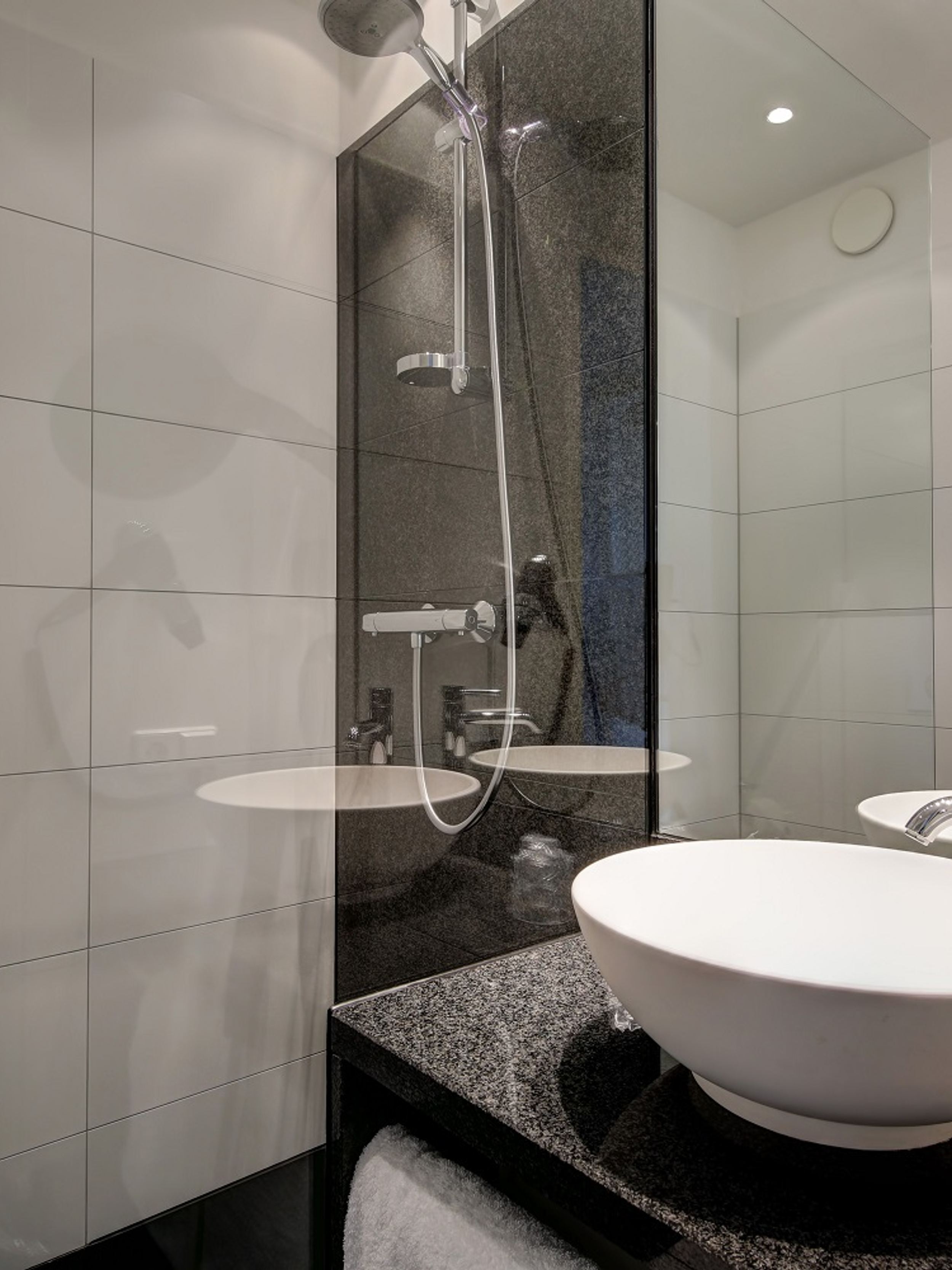 Hotelbadezimmer mit großzügiger Dusche, rundem Waschbecken auf Granitplatte und Haartrockner an der Wand, ideal für komfortable Erfrischung und Pflege während des Aufenthalts.