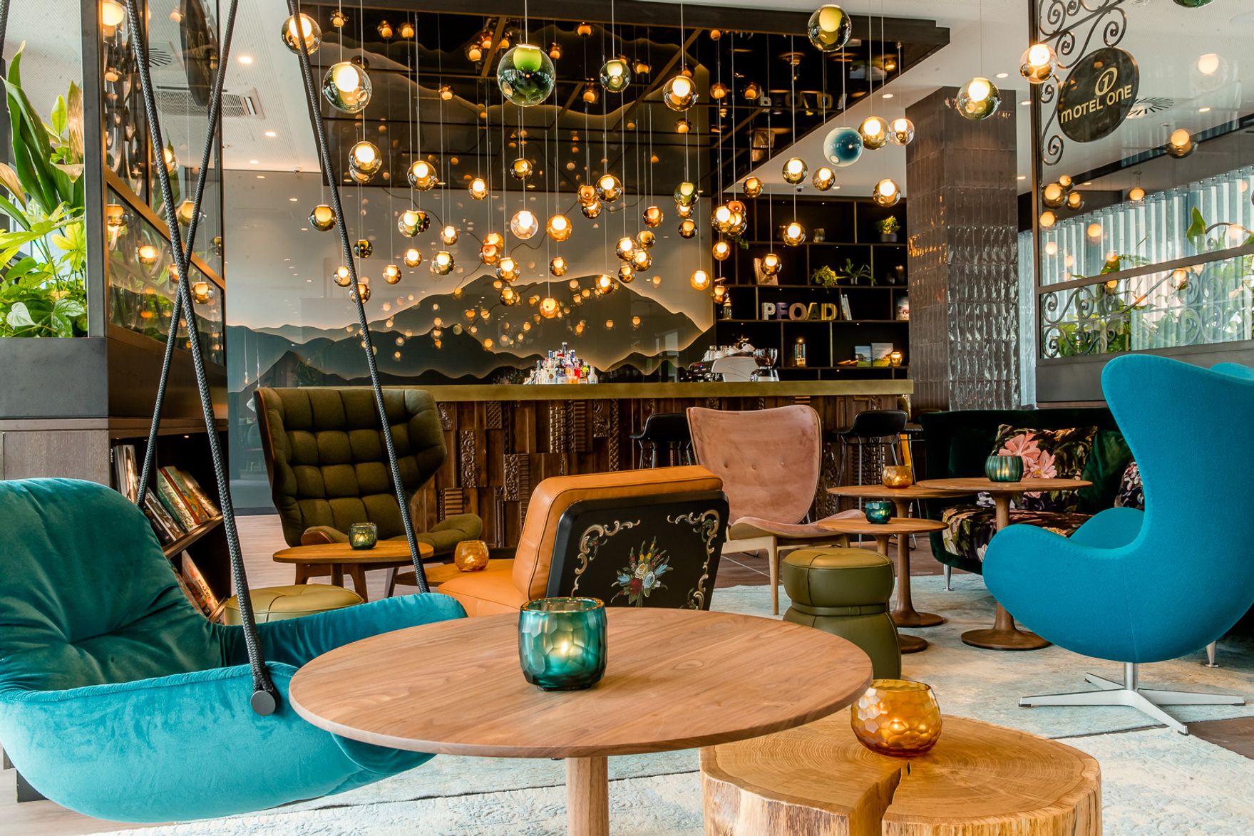 Gemütliche, stilvoll eingerichtete Lounge mit modernen Sesseln, Holz- und Steintischen sowie warmen Hängelampen, die eine einladende Atmosphäre schaffen – ideal zum Entspannen und geselligen Beisammensein.