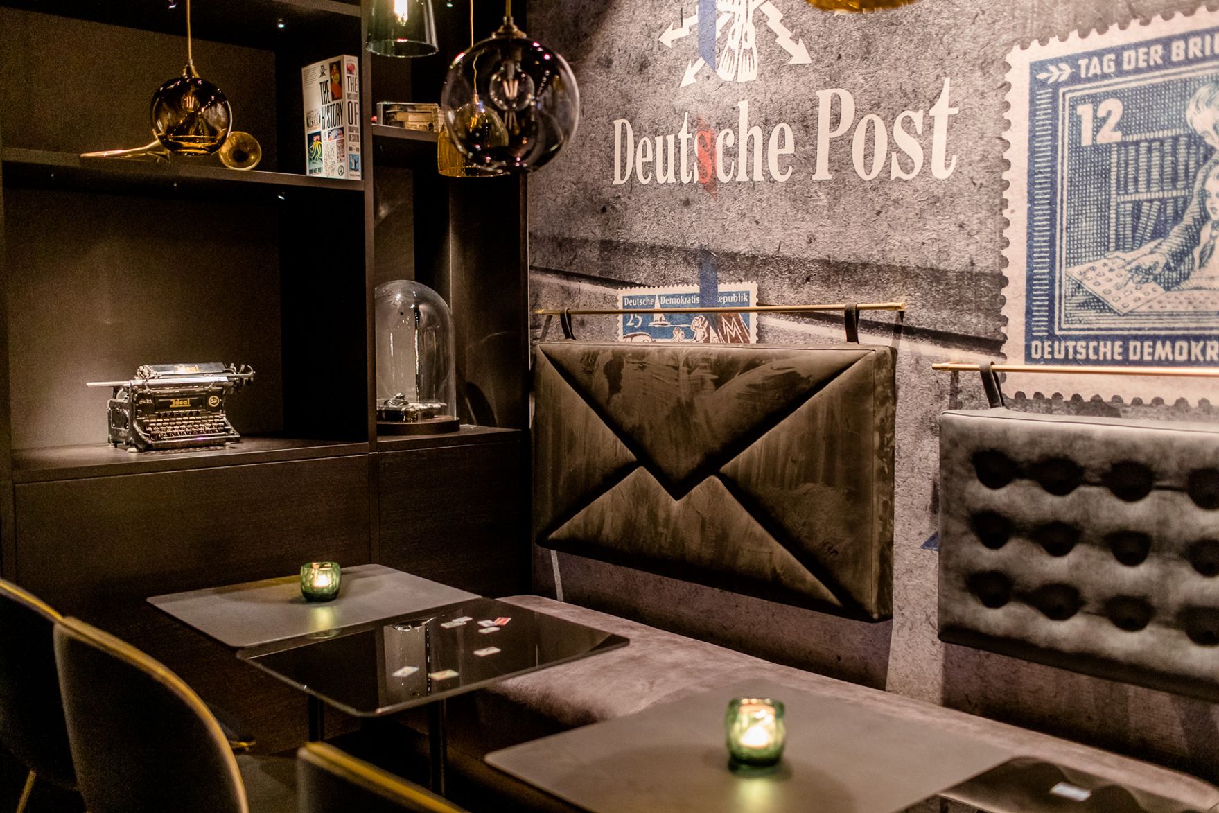 Gemütliche Sitzecke mit gepolsterten Bänken, Kerzenlicht und nostalgischer Wandgestaltung mit Briefmarkenmotiv, ideal für entspannte Pausen in stilvollem Ambiente.