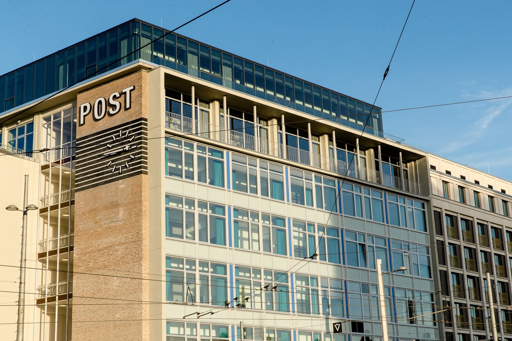 Hotel Leipzig Post Motel One Gebäude mit großflächigen Fenstern und markanter Fassade, auf der das Wort „POST“ und eine stilisierte Uhr sichtbar sind. Idealer Standort im urbanen Umfeld, der Komfort und zeitgemäßes Design vereint.