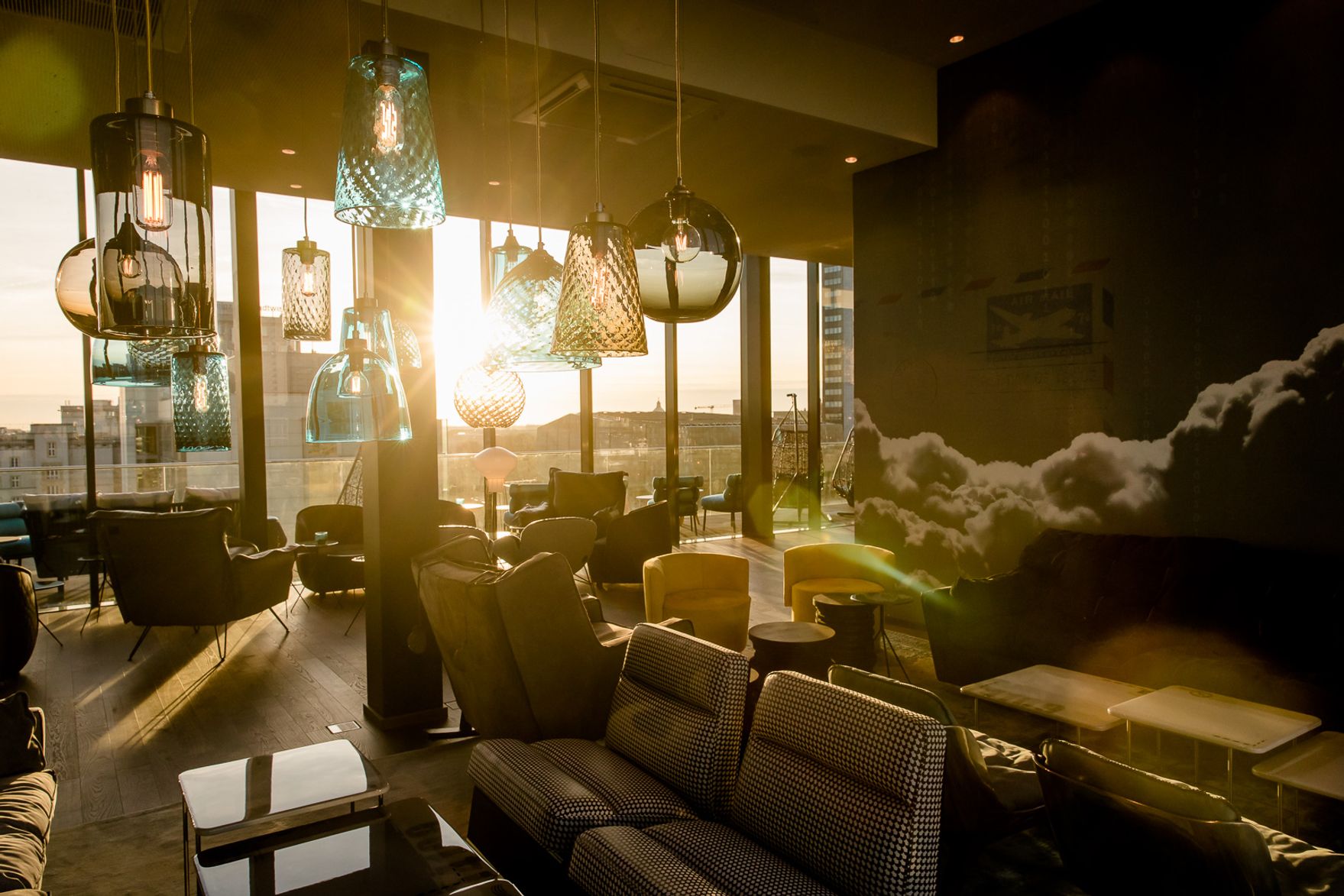 Lichtdurchfluteter Lounge-Bereich mit gemütlichen Sitzmöbeln und Designerlampen, die bei Sonnenuntergang eine warme, einladende Atmosphäre schaffen, ideal zum Entspannen und Verweilen.