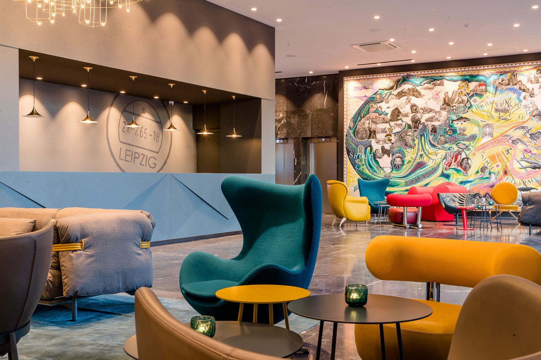 Moderne Hotel-Lounge mit farbenfrohen Sesseln und Sofas, stilvollen Tischen und einer großen, lebhaften Wandkunst. Helles, einladendes Ambiente für Entspannung und geselliges Beisammensein im Zentrum von Leipzig.