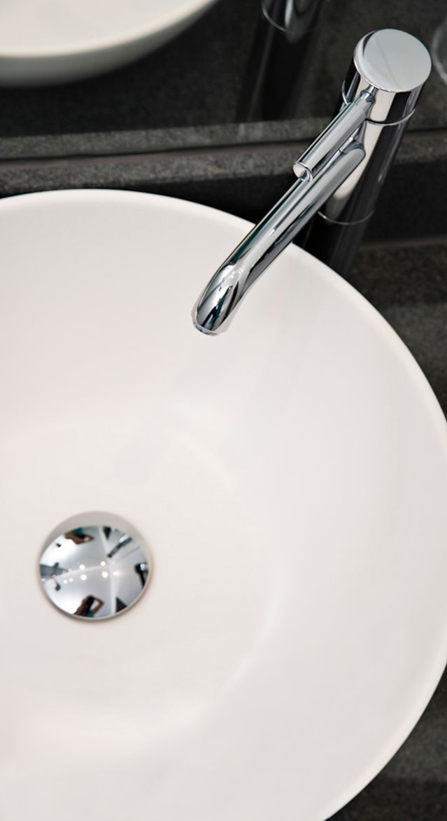 Moderner, runder weißer Waschtisch mit elegantem, chromglänzendem Einhebelmischer vor dunklem Hintergrund, ideal für stilvolles Badezimmerambiente.
