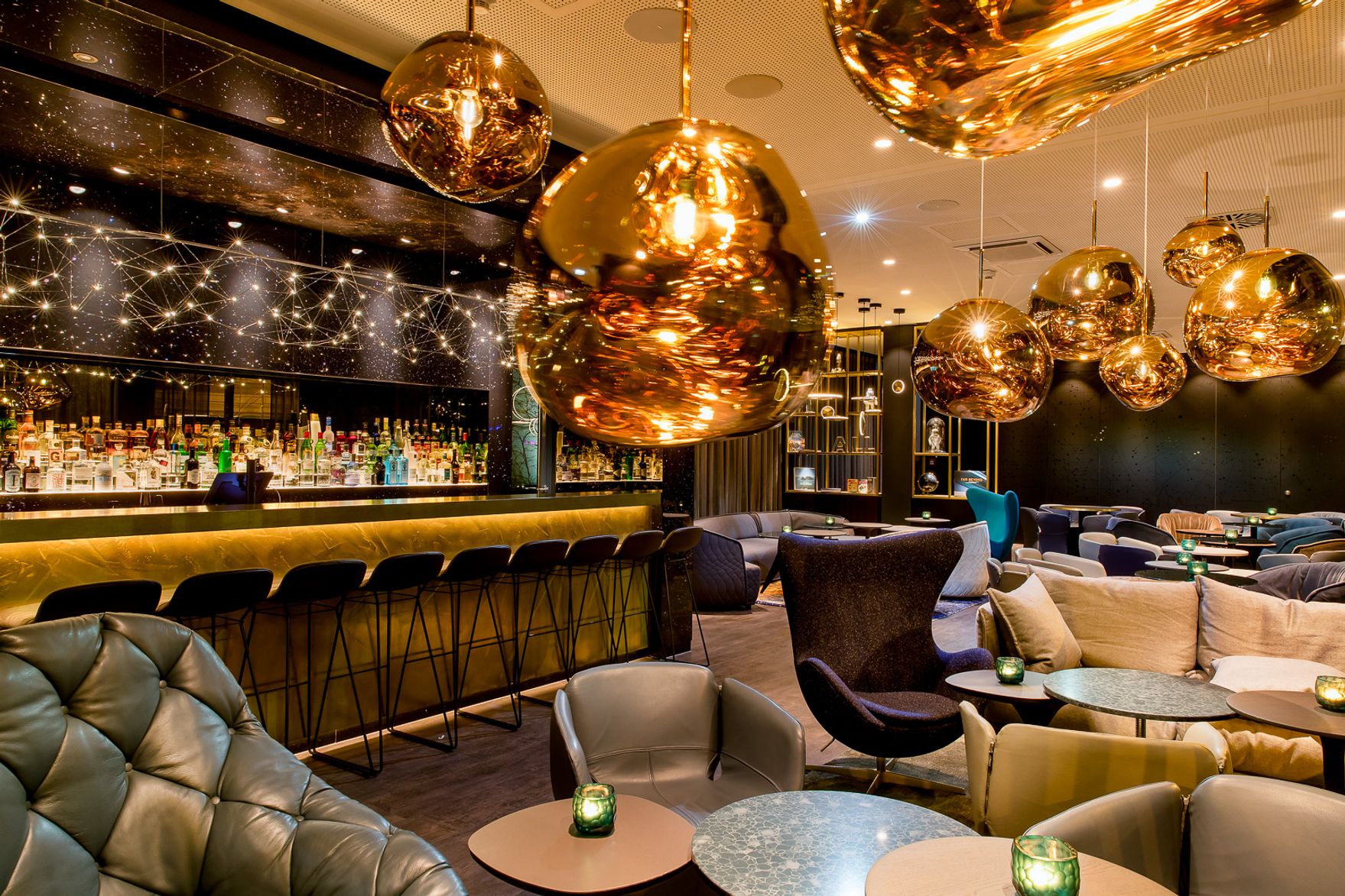 Stilvolle Hotelbar mit gemütlichen Sitzgelegenheiten, warmem Licht durch goldene Pendelleuchten und elegantem Ambiente, ideal für entspannte Abende und gesellige Treffen.