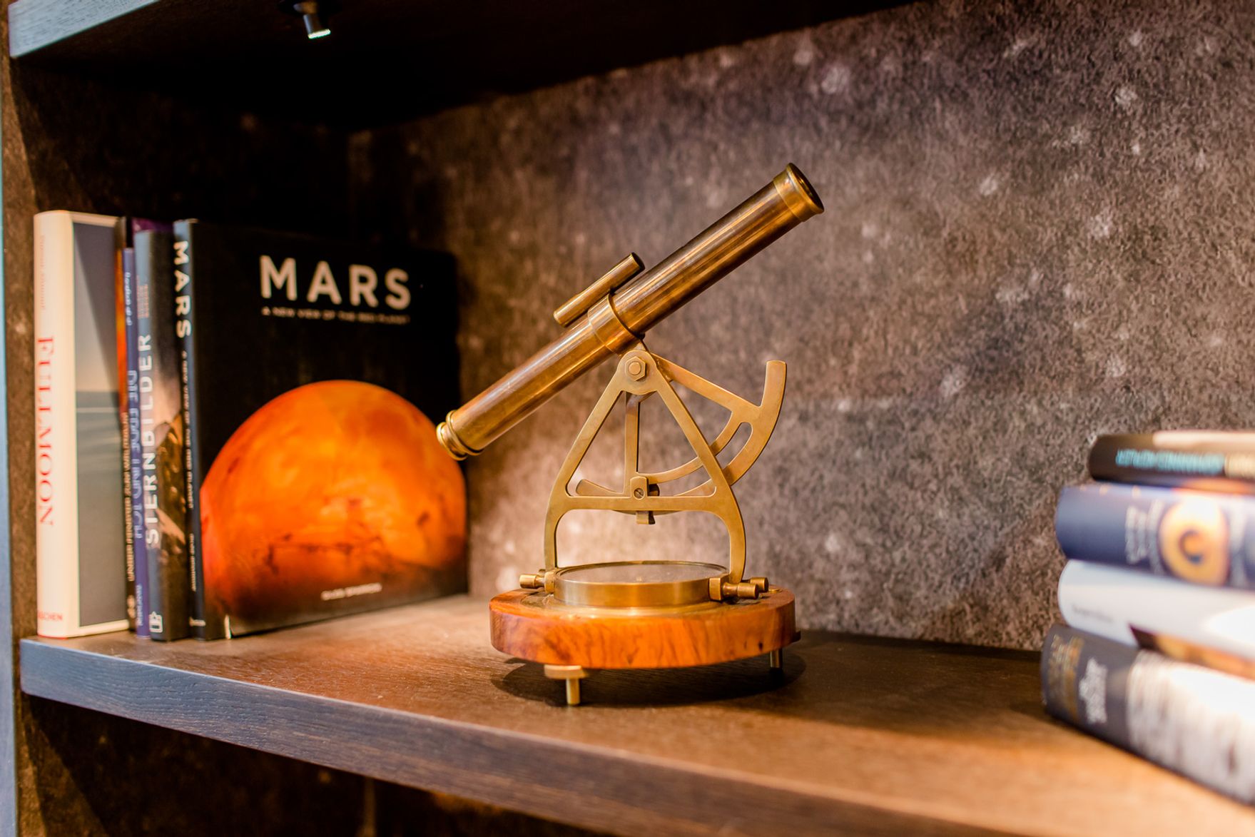Antike Messing-Sextant auf Holzsockel steht auf einem Regal neben Büchern, darunter ein Buch mit dem Titel „Mars“ und einem Bild des Planeten Mars.