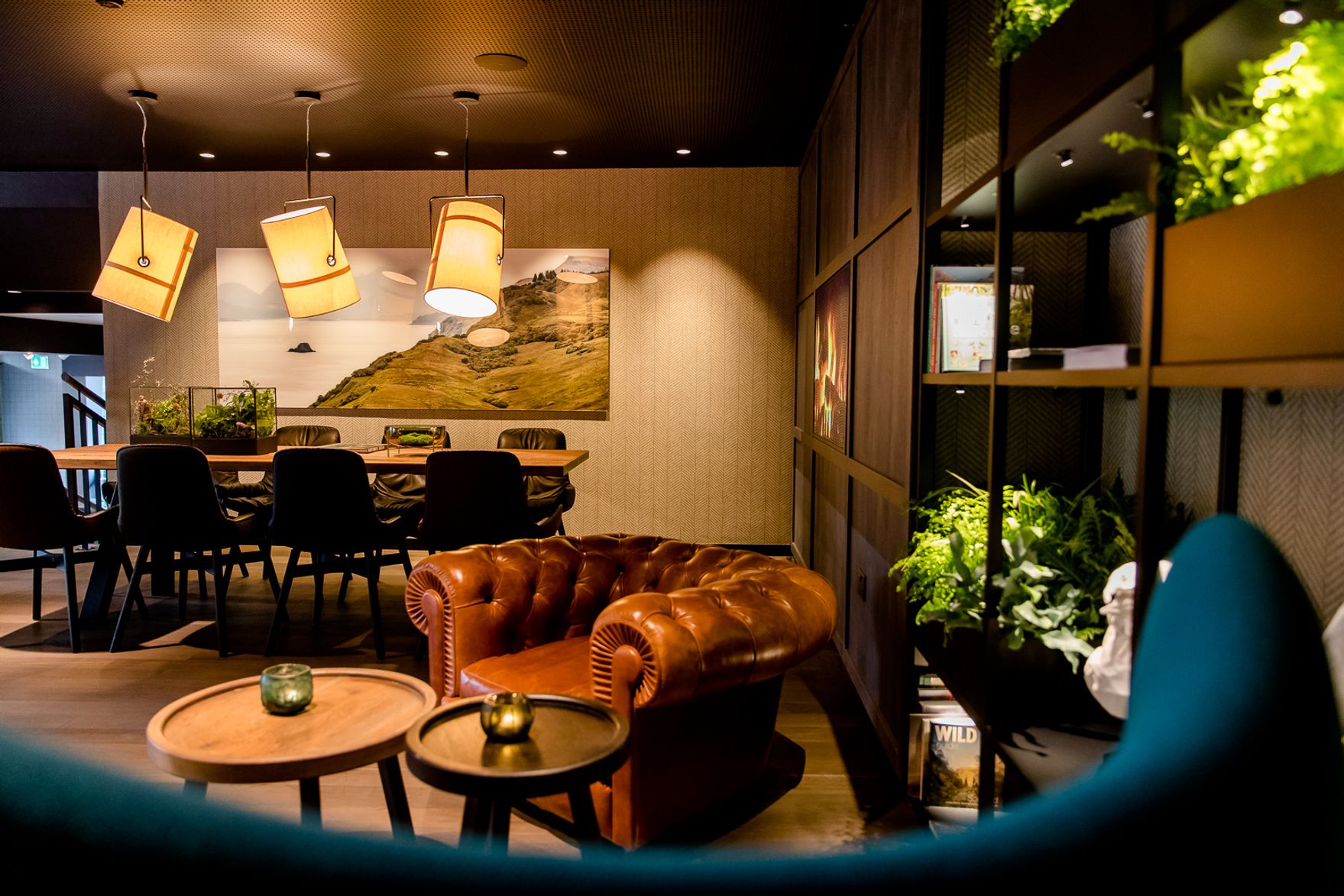 Gemütlicher Lounge-Bereich mit braunem Ledersessel, moderner Holzdecke, stilvollen Hängeleuchten und großen Tischen, umgeben von Pflanzen für eine entspannte Atmosphäre.