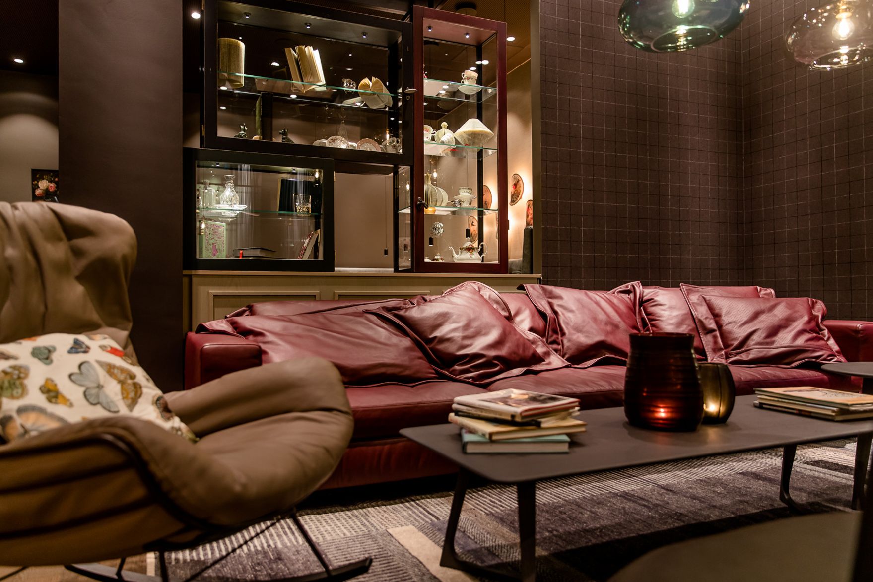 Gemütlicher Lounge-Bereich mit rotem Ledersofa, bequemen Sesseln und dekorativem Couchtisch, umgeben von warmem Licht und stilvollen Vitrinen mit Kunstobjekten. Ideal zum Entspannen und Lesen.