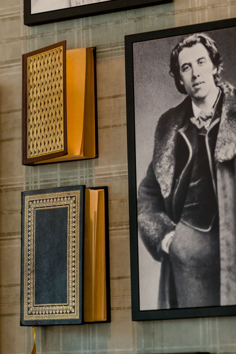 Zwei dekorative, zum Teil geöffnete Bücher an einer Wand neben einem schwarz-weißen Porträt eines Mannes in historischem Kleidungsstil.