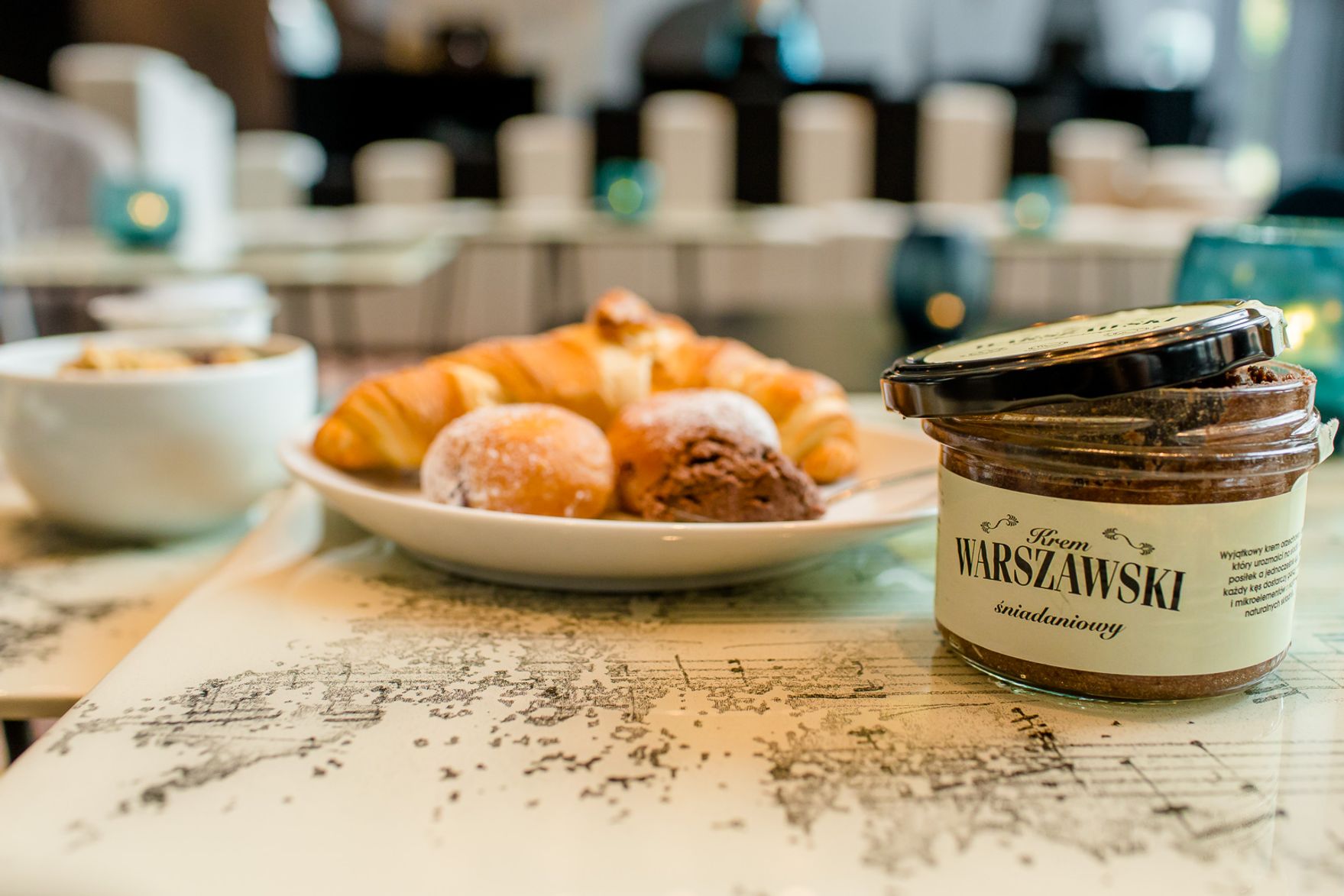 Glas mit Frühstücksmarmelade neben einem Teller mit Croissants und Brötchen, serviert auf einem Tisch mit einer dekorativen Landkarte. Gemütliche Atmosphäre für ein entspanntes Frühstück im Hotel.