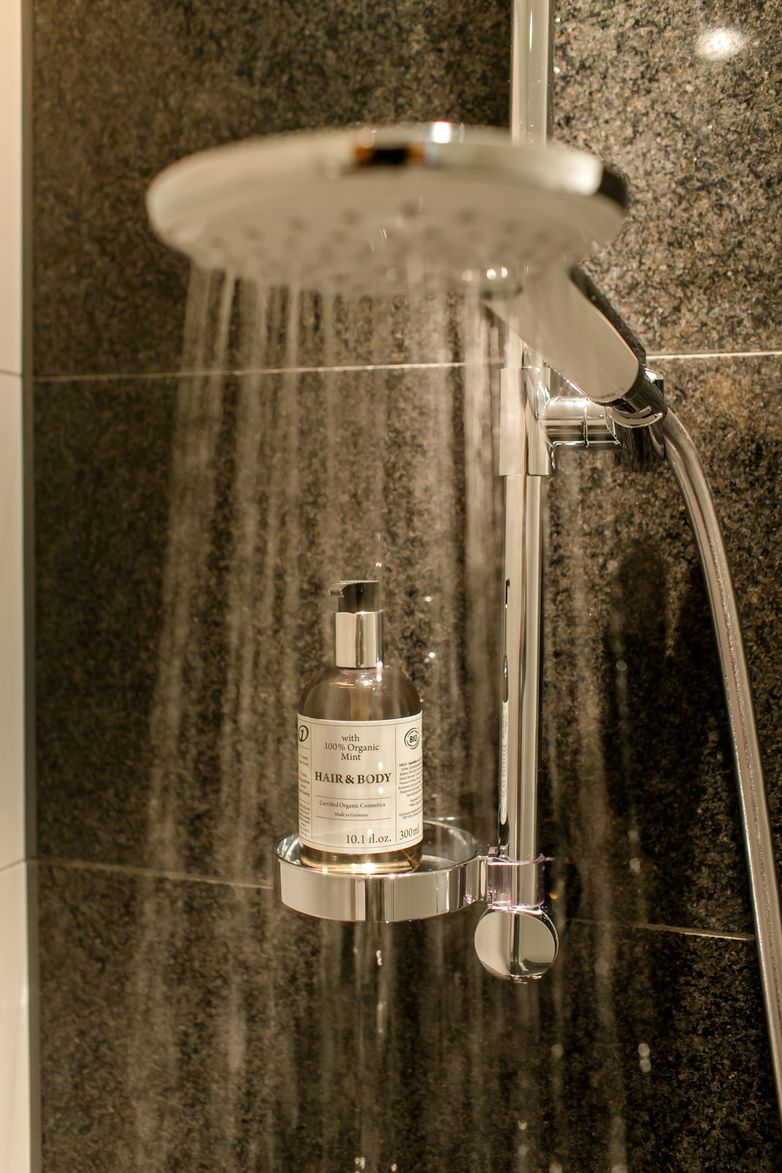 Regendusche mit fließendem Wasser vor dunkler Steinwand, dekorativ eingerichteter Duschbereich mit hochwertigem Pflegeprodukt.