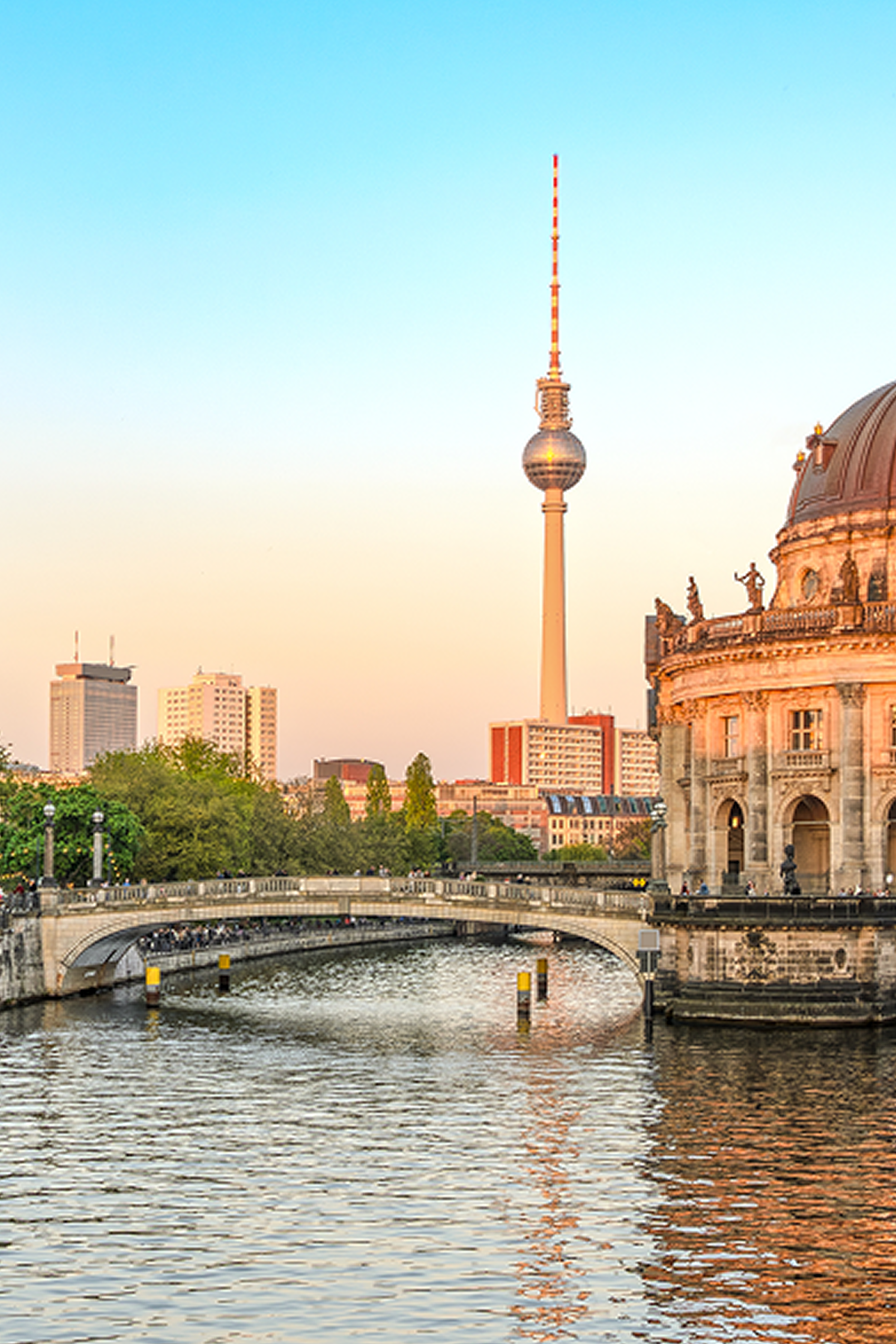 Blick auf die Spree mit historischer Bogenbrücke, dem Berliner Bodemuseum rechts und dem Fernsehturm im Hintergrund bei klarem Himmel.