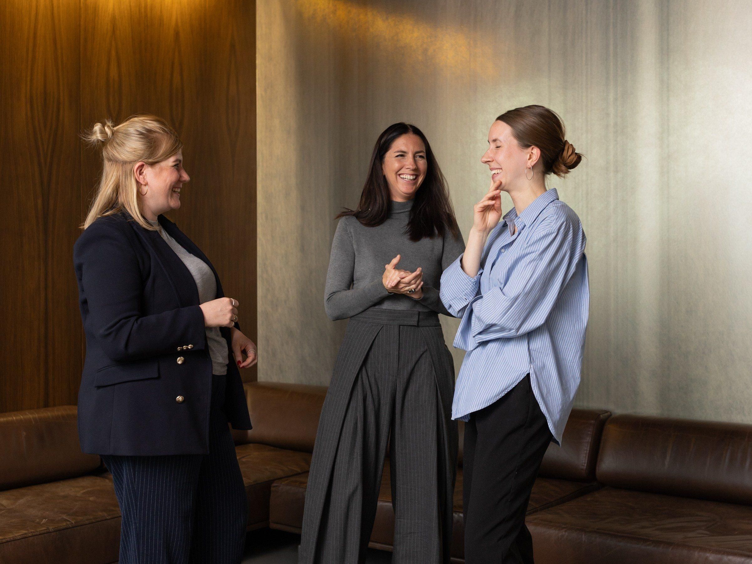 Das Foto zeigt drei Frauen, die in einem Halbkreis stehen und ein Gespräch führen und über etwas lachen.