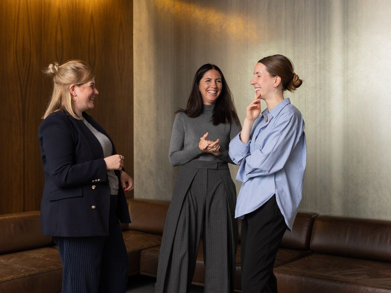 Das Foto zeigt drei Frauen, die in einem Halbkreis stehen und ein Gespräch führen und über etwas lachen.