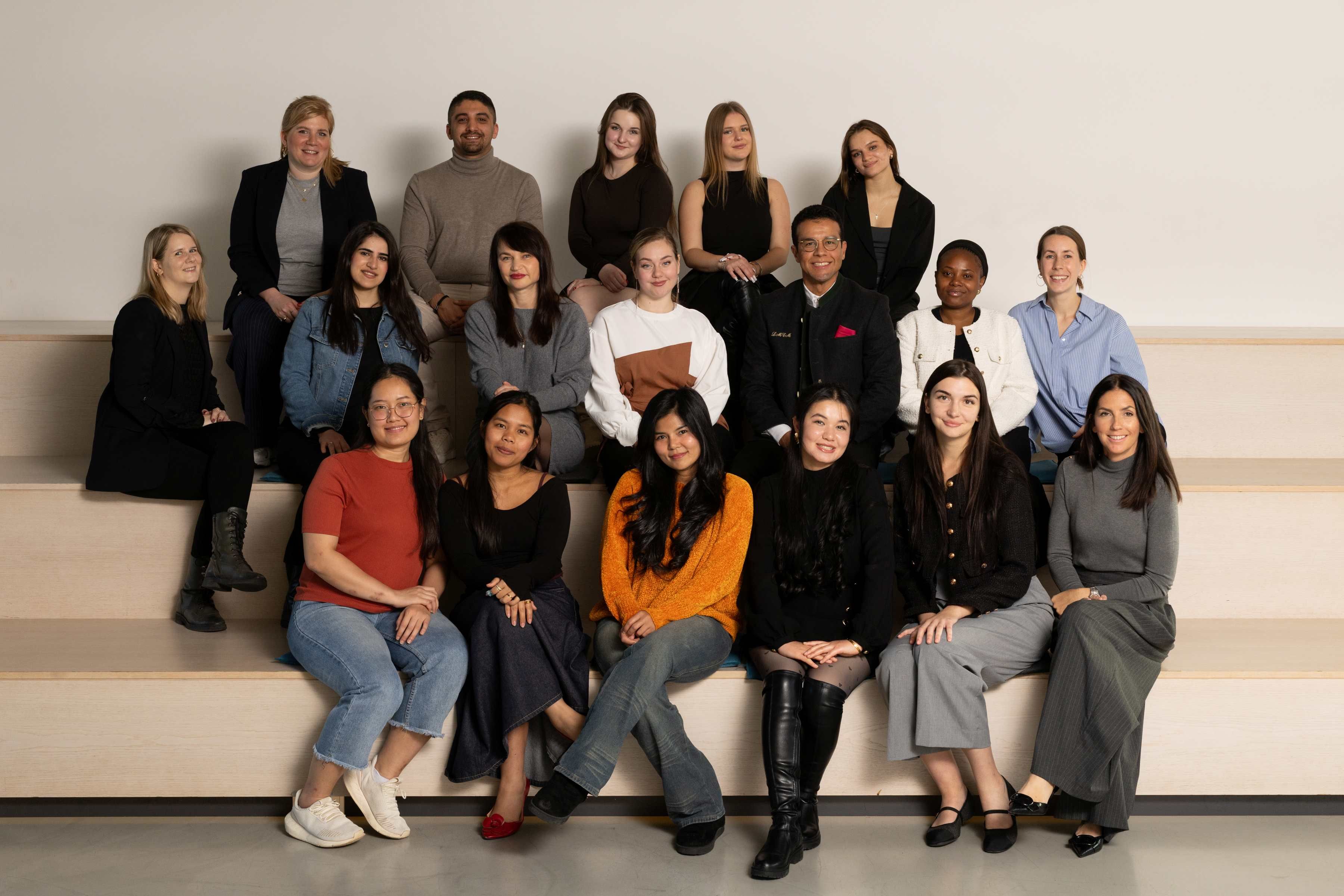 Gruppenbild von 16 Personen unterschiedlichen Alters und verschiedener Herkunft, die entspannt und freundlich in einer hellen Umgebung zusammensitzen.