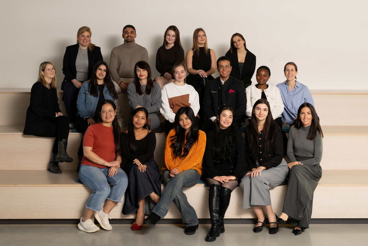 Gruppenbild von 16 Personen unterschiedlichen Alters und verschiedener Herkunft, die entspannt und freundlich in einer hellen Umgebung zusammensitzen.