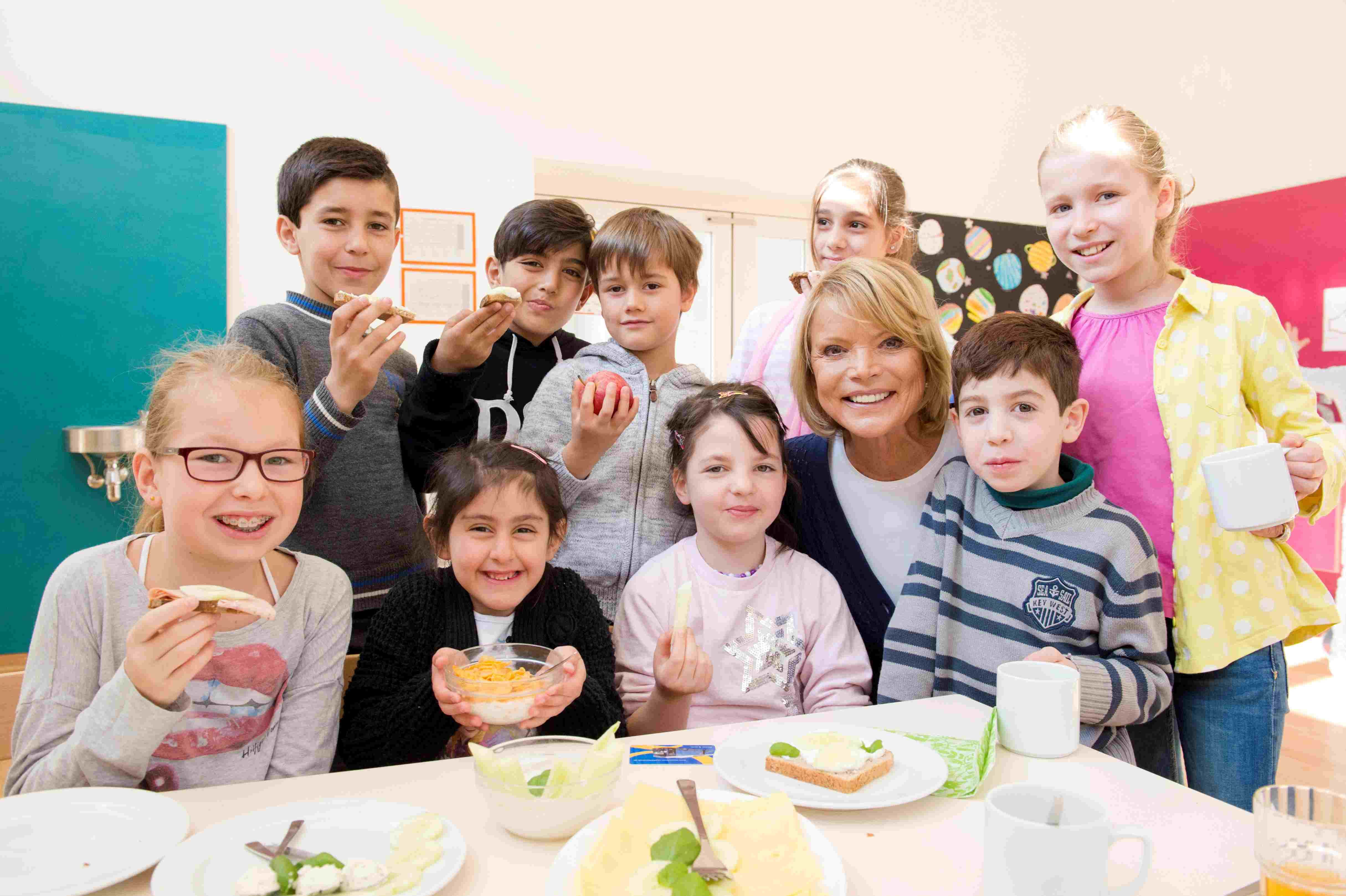 Eine fröhliche Gruppe von Kindern und einer erwachsenen Frau sitzt gemeinsam an einem Tisch und genießt gesunde Snacks in einer hellen, freundlichen Umgebung. Eine fröhliche Gruppe von Kindern und einer erwachsenen Frau sitzt gemeinsam an einem Tisch und genießt gesunde Snacks in einer hellen, freundlichen Umgebung.